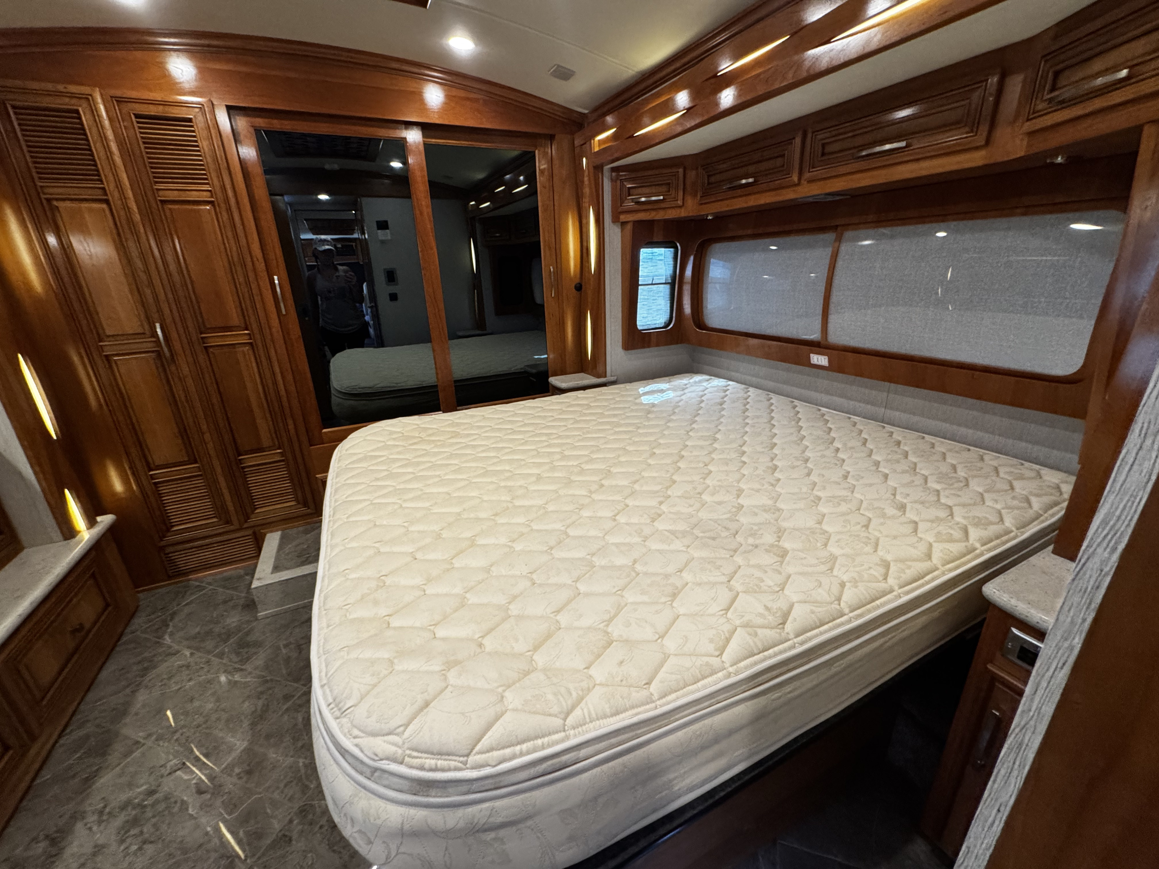 This RV rental bedroom features a large, comfortable bed with quilted mattress, rich wood cabinetry, and reflective mirror. Ideal for travel.. New Aire New Aire Motorhome 2020