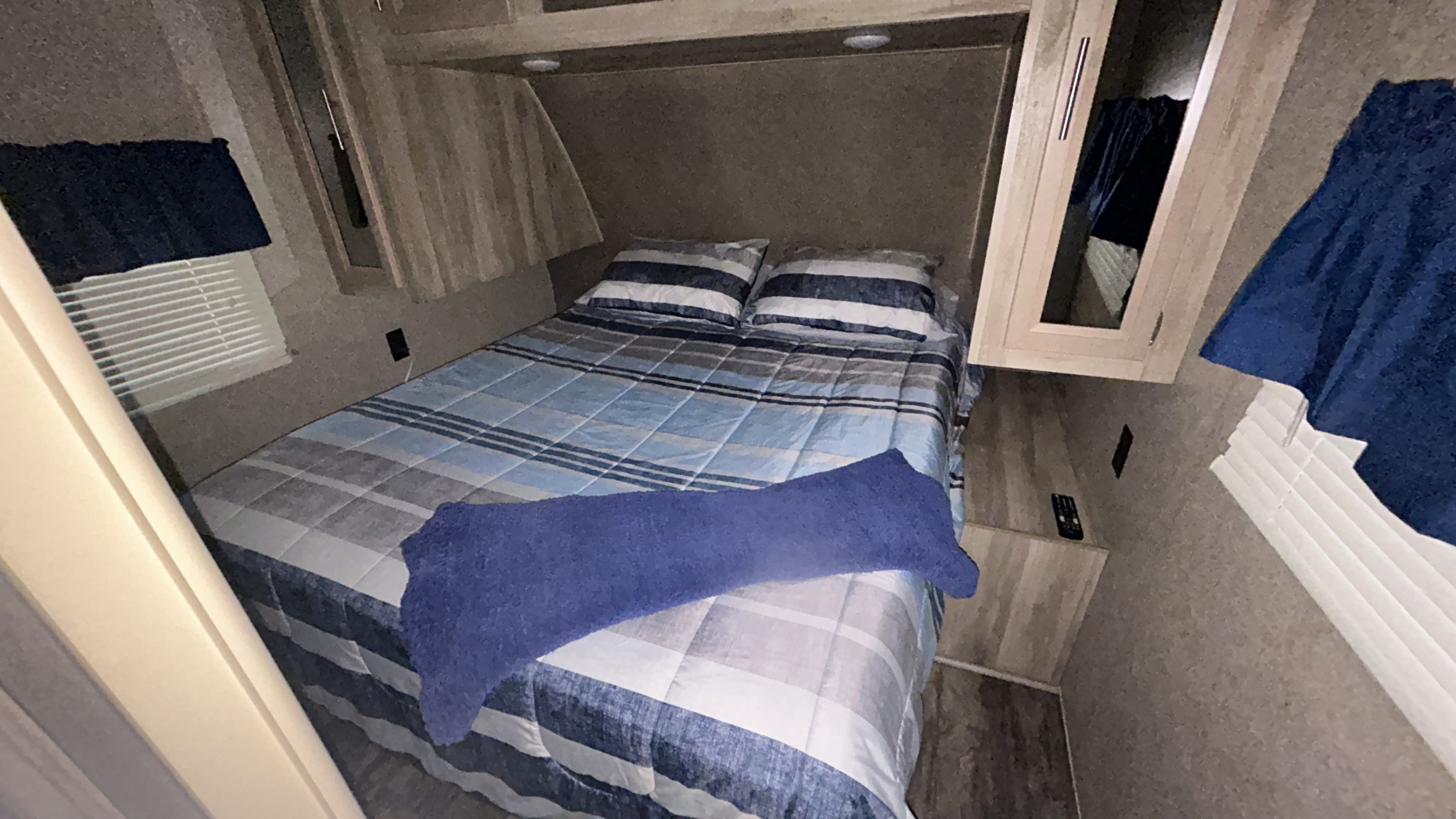 This cozy RV rental bedroom offers a comfortable striped bed, overhead storage, and a window for pleasant stays.. Coachmen Catalina 2019
