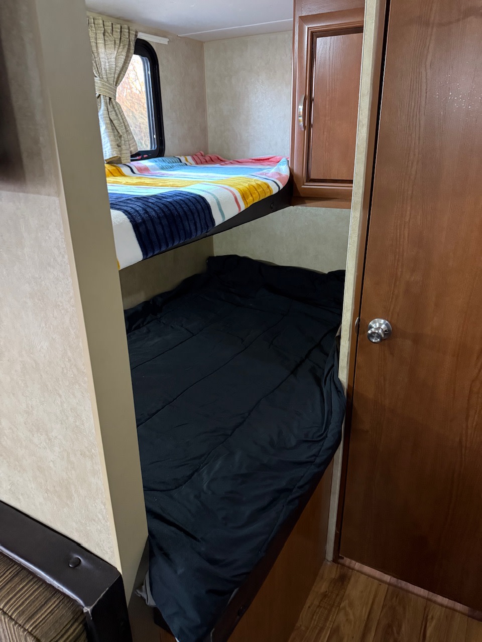 Cozy RV rental bunk bed area: an upper bunk with colorful bedding and a lower bunk with black bedding. Includes a window & storage.. Forest River Wildwood X-Lite 2015