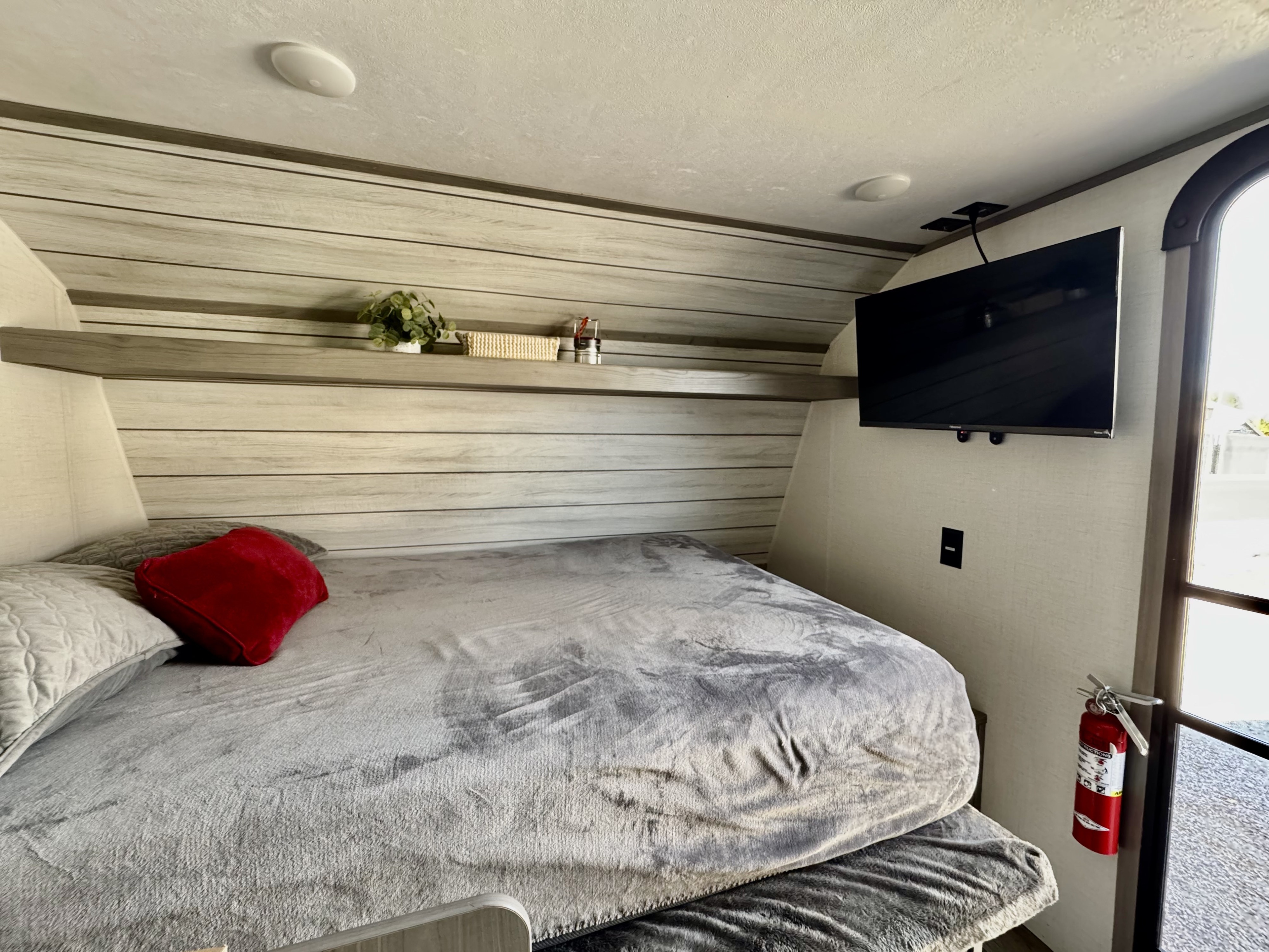 Cozy RV rental bedroom: features a comfortable bed, mounted TV, decorative shelf, and a fire extinguisher for safety.. Dutchmen Coleman Lantern LT 2023