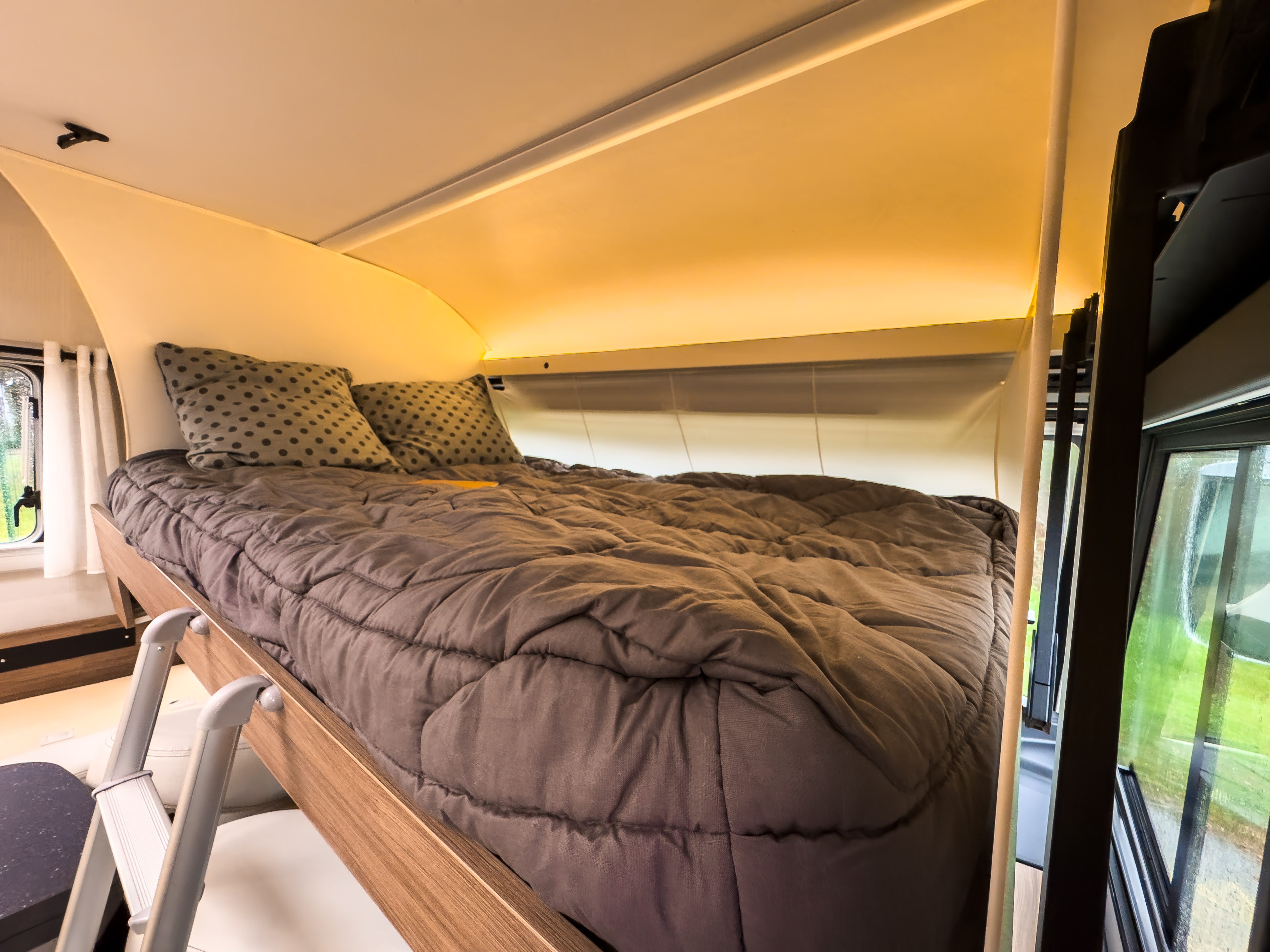 Warm and inviting elevated bed in an RV rental interior, complete with soft bedding, ambient lighting, and an access ladder.. Pilote G 740 FC EVIDENCE 2023