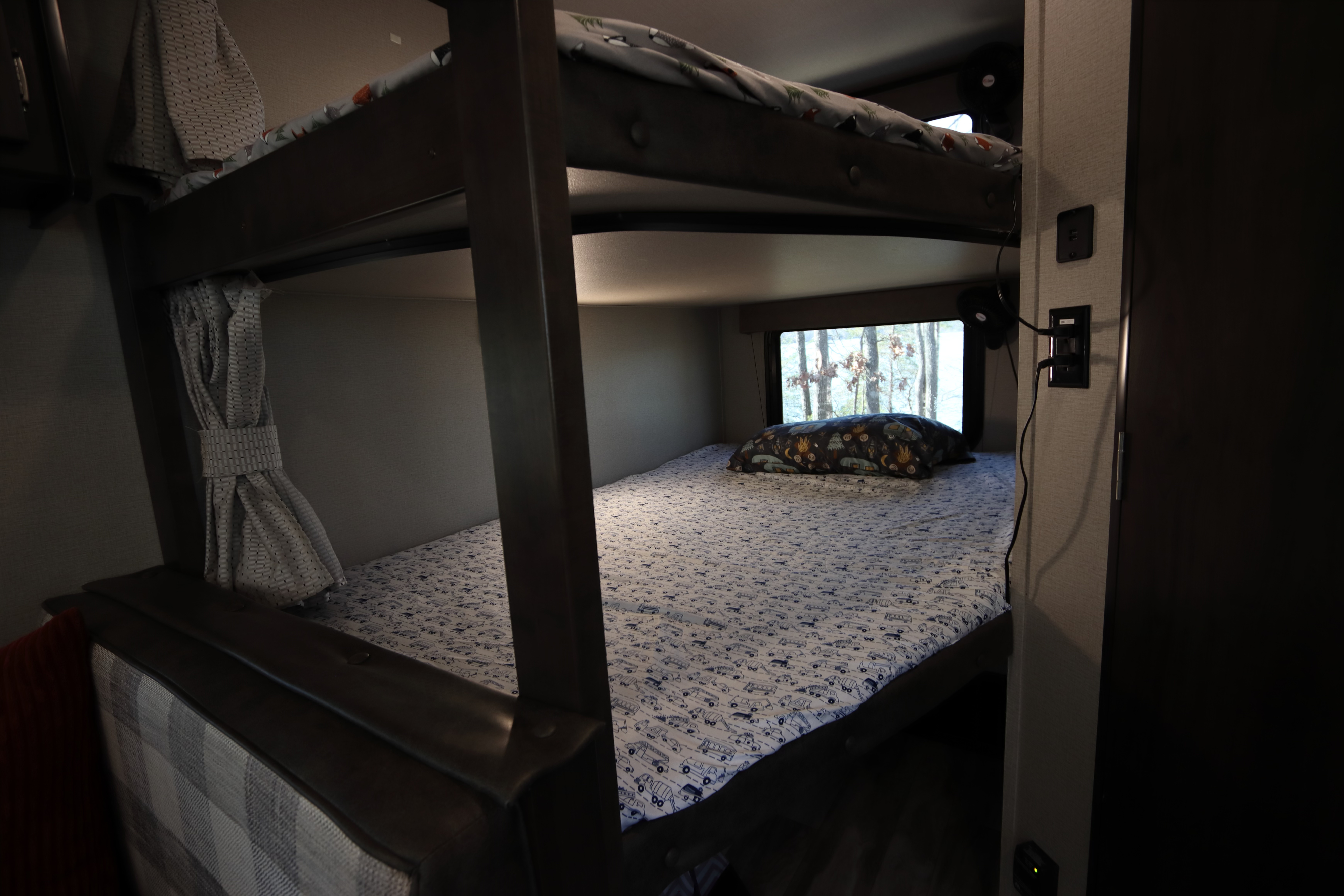 Cozy RV rental bunk beds, perfect for family adventures. Features vehicle-patterned sheets & window views.. Grand Design Transcend Xplor 2020