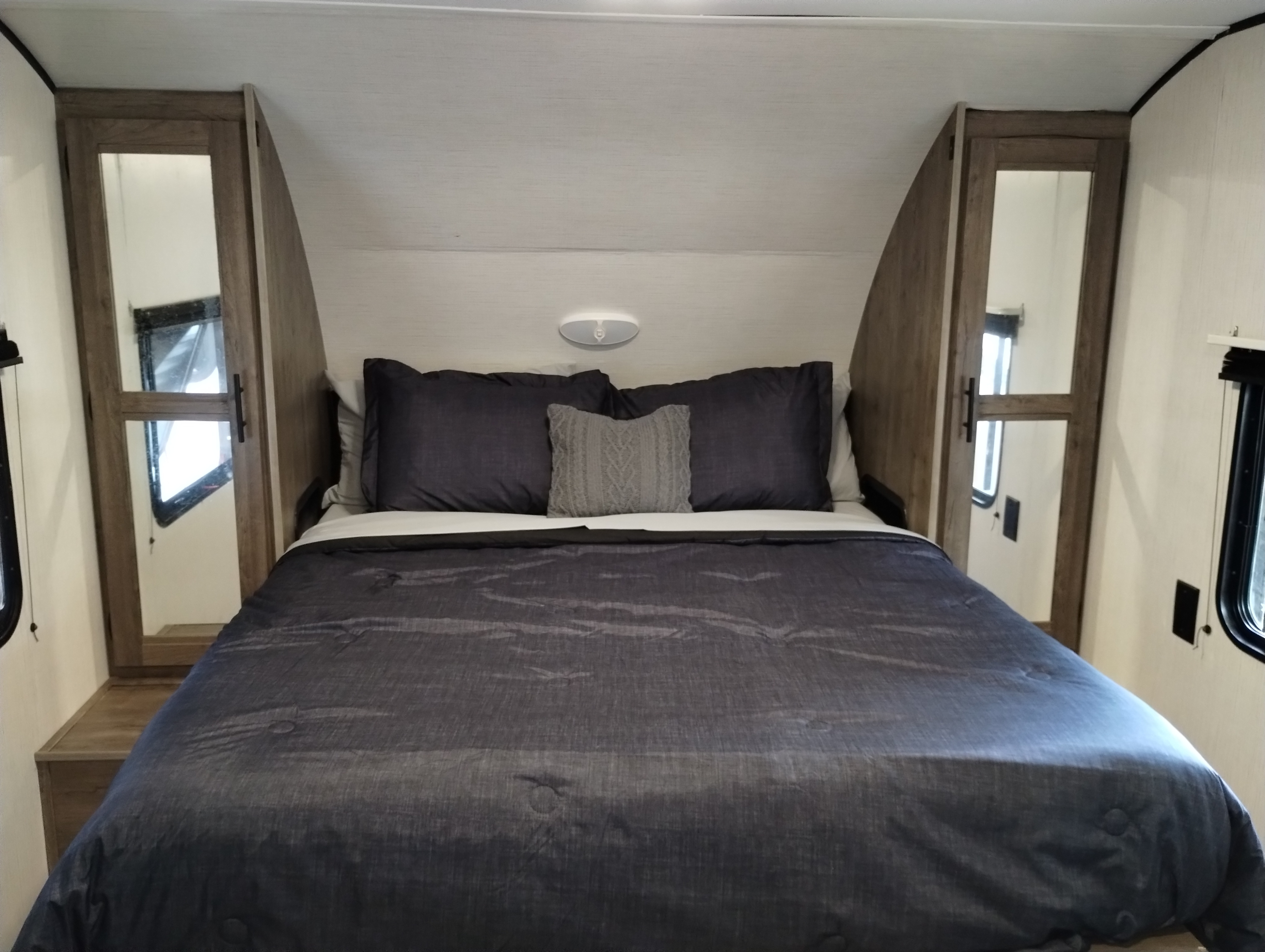 Cozy RV rental bedroom with dark gray bedding, mirrored cabinets, and a comfortable bed.. Heartland RVs Pioneer RB215 2022