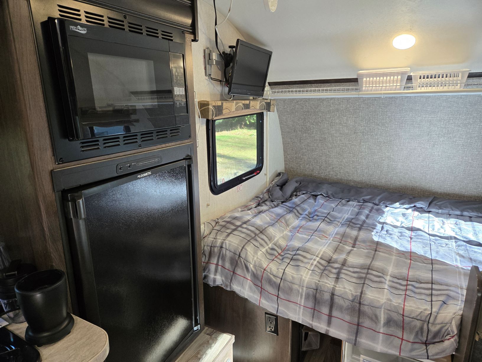 RV rental interior: compact kitchen (microwave, fridge), wall-mounted TV, comfy plaid bed, overhead storage.. Starcraft Satellite 2019