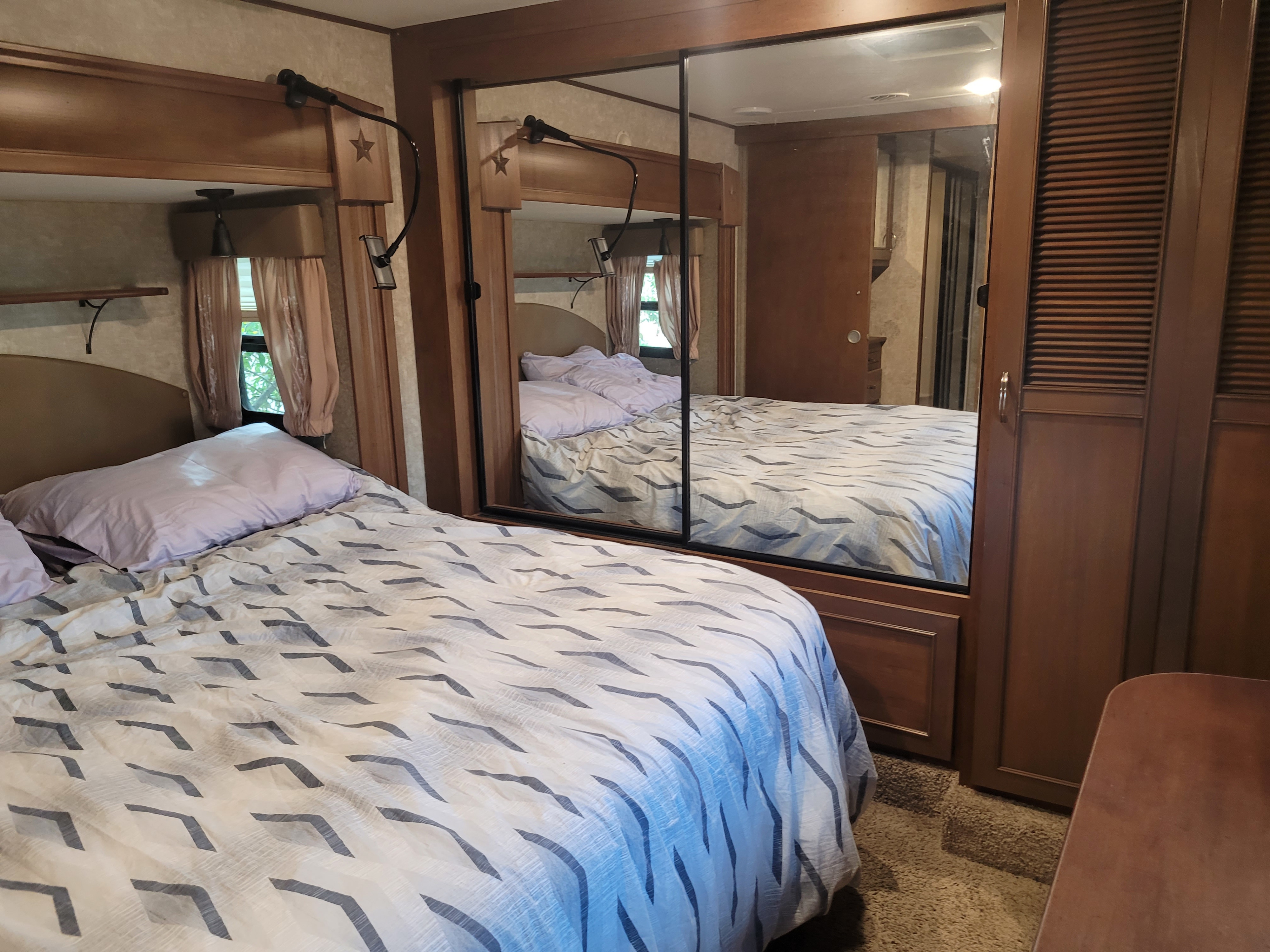 This RV rental bedroom offers a comfortable bed with patterned covers, a mirrored closet, and window views.. Open Range RV Open Range RV Fifth Wheel 2015