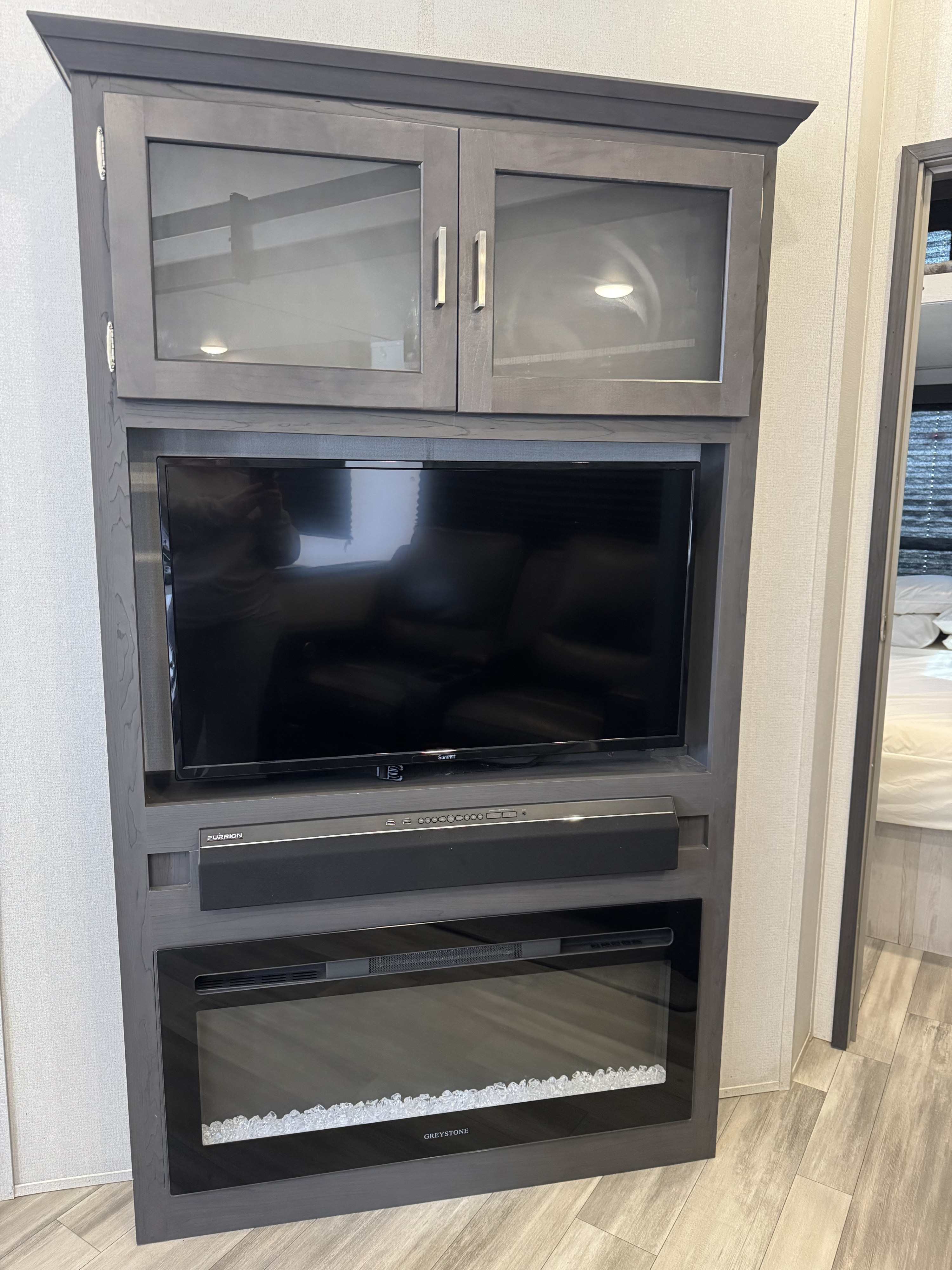 RV rental entertainment center with a TV, soundbar, and electric fireplace, set in a modern gray built-in unit.. Keystone Sunset Trail 2022
