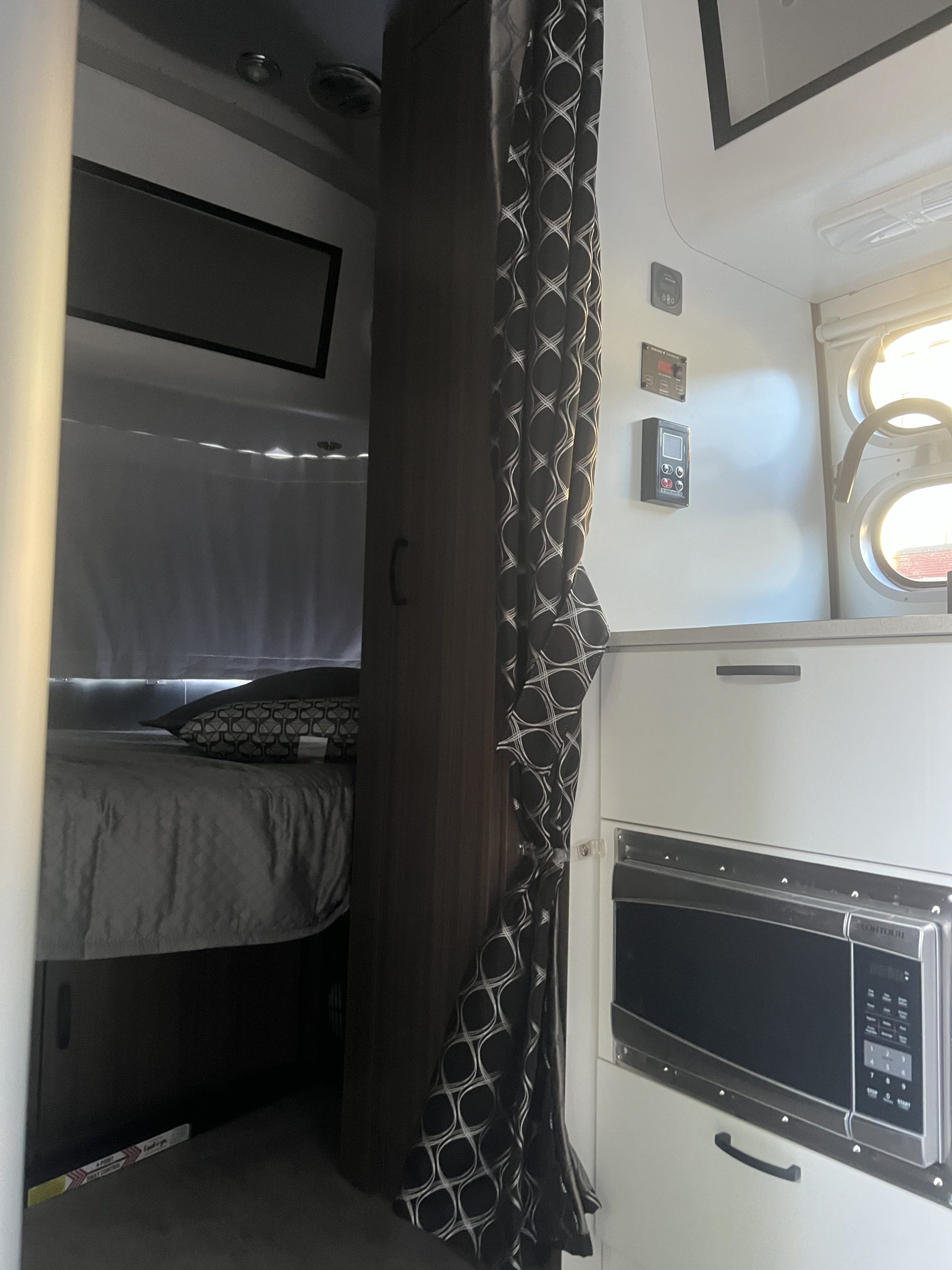 RV rental interior: A cozy bed area, dark cabinet divider, and a kitchen zone with microwave and control panels.. Airstream Caravel 2022