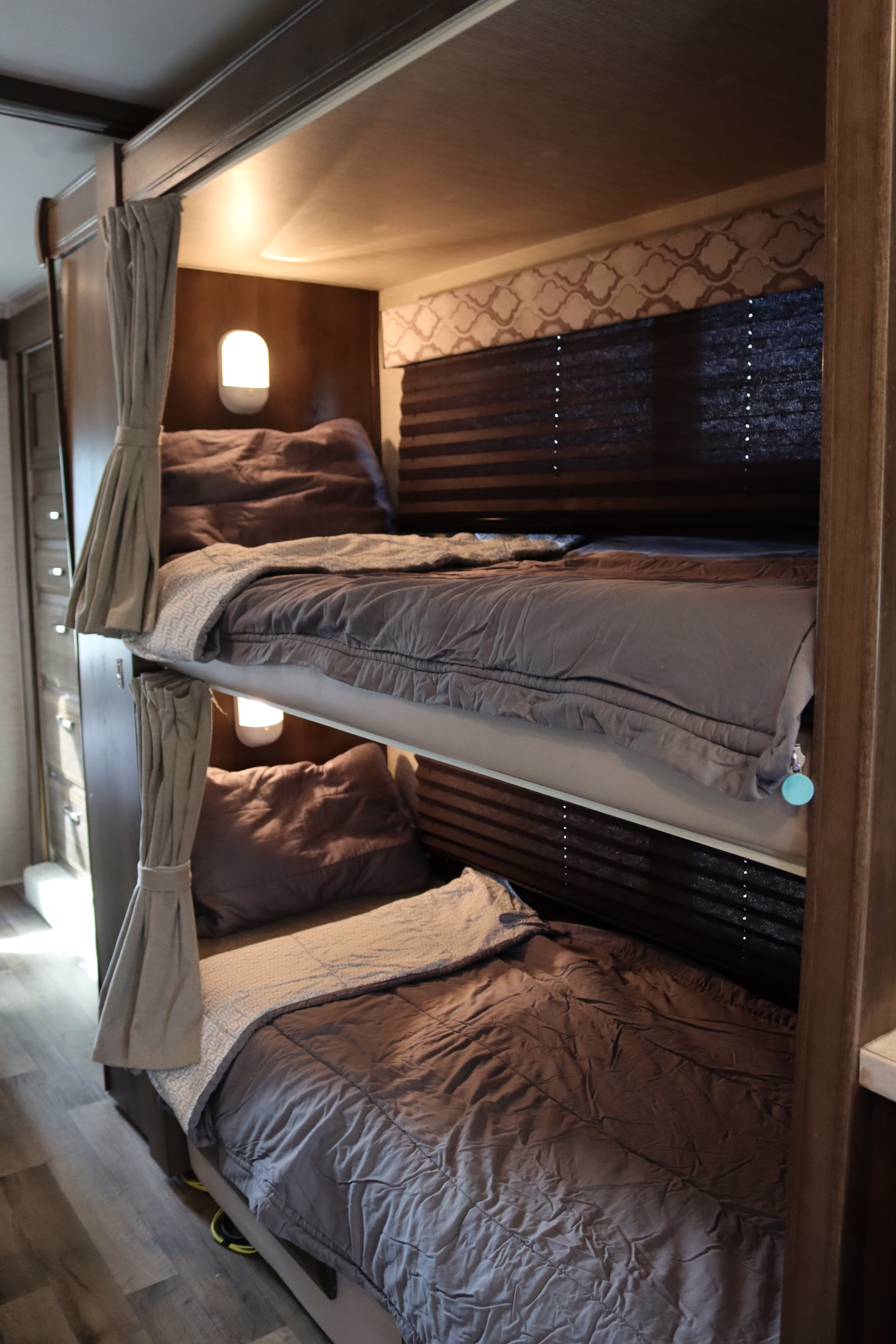 An RV rental's sleeping area with two neatly made bunk beds, complete with cozy bedding, lights, and privacy shades.. Jayco Redhawk 2021
