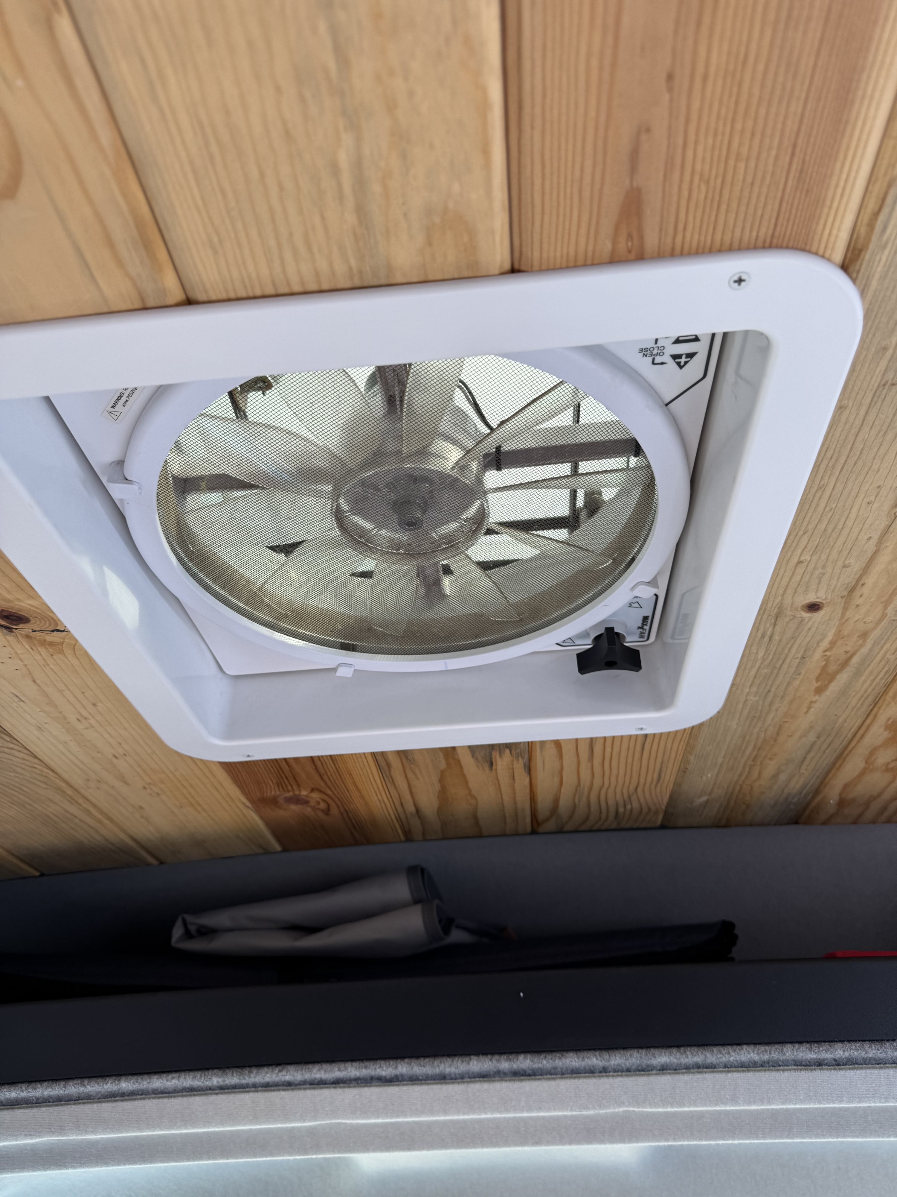An interior view of an RV rental showing a white ceiling fan with a mesh screen against wood paneling, offering air circulation.. Dave and Matt Vans LV7 Ram Promaster 3500 2022