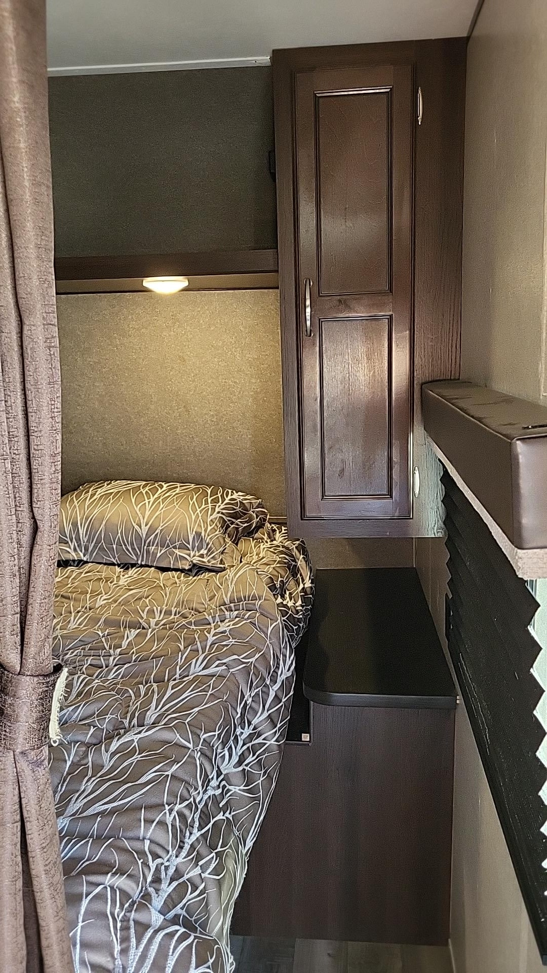 RV rental interior: Comfortable bed with tree-patterned linen, overhead light, and dark wood storage cabinet in a compact space.. Jayco Jay Flight 2018