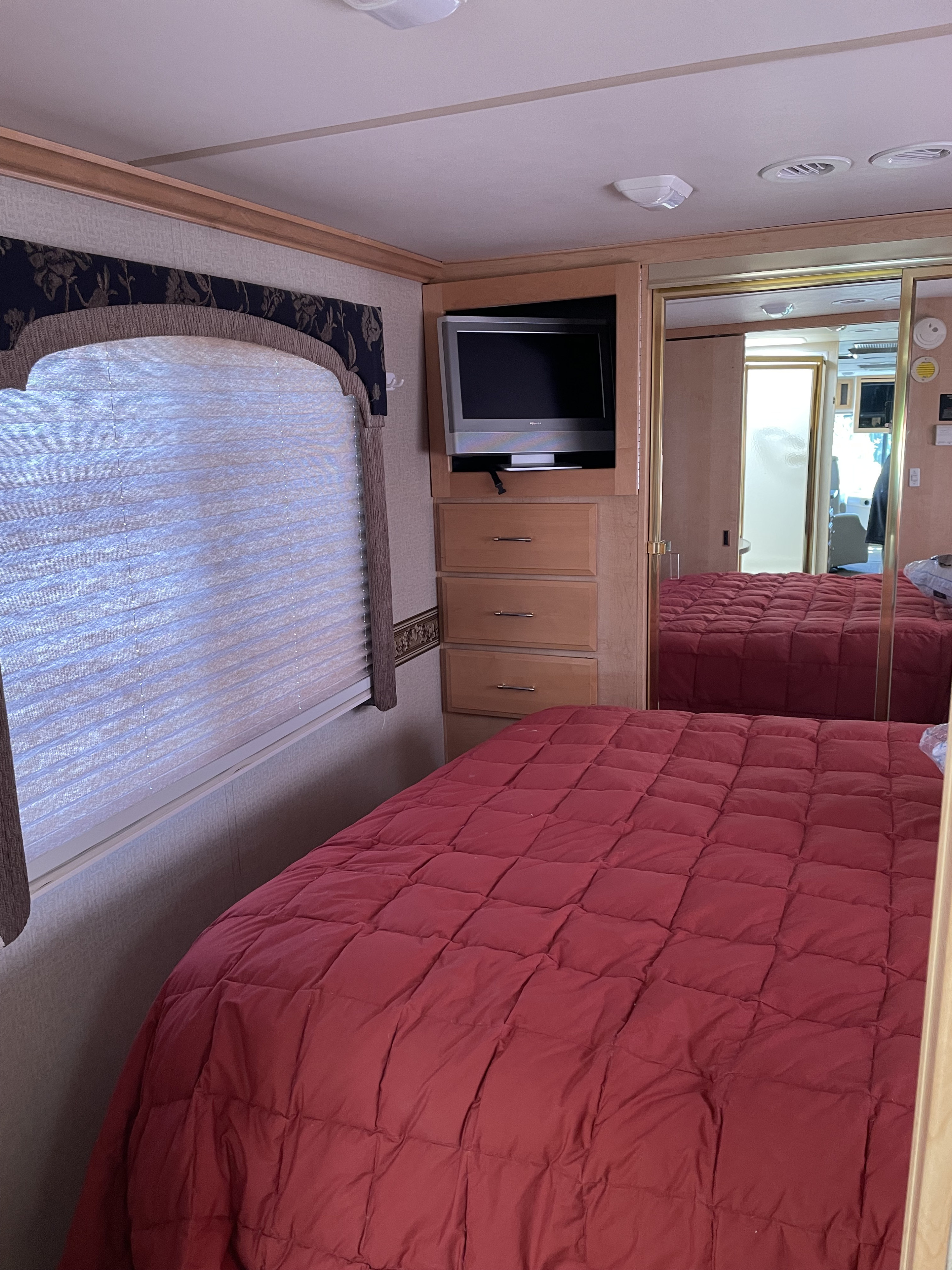 Cozy RV rental bedroom featuring a red bed, built-in TV/storage, mirrored closet doors, and window blinds.. Fleetwood Bounder 37U 2003