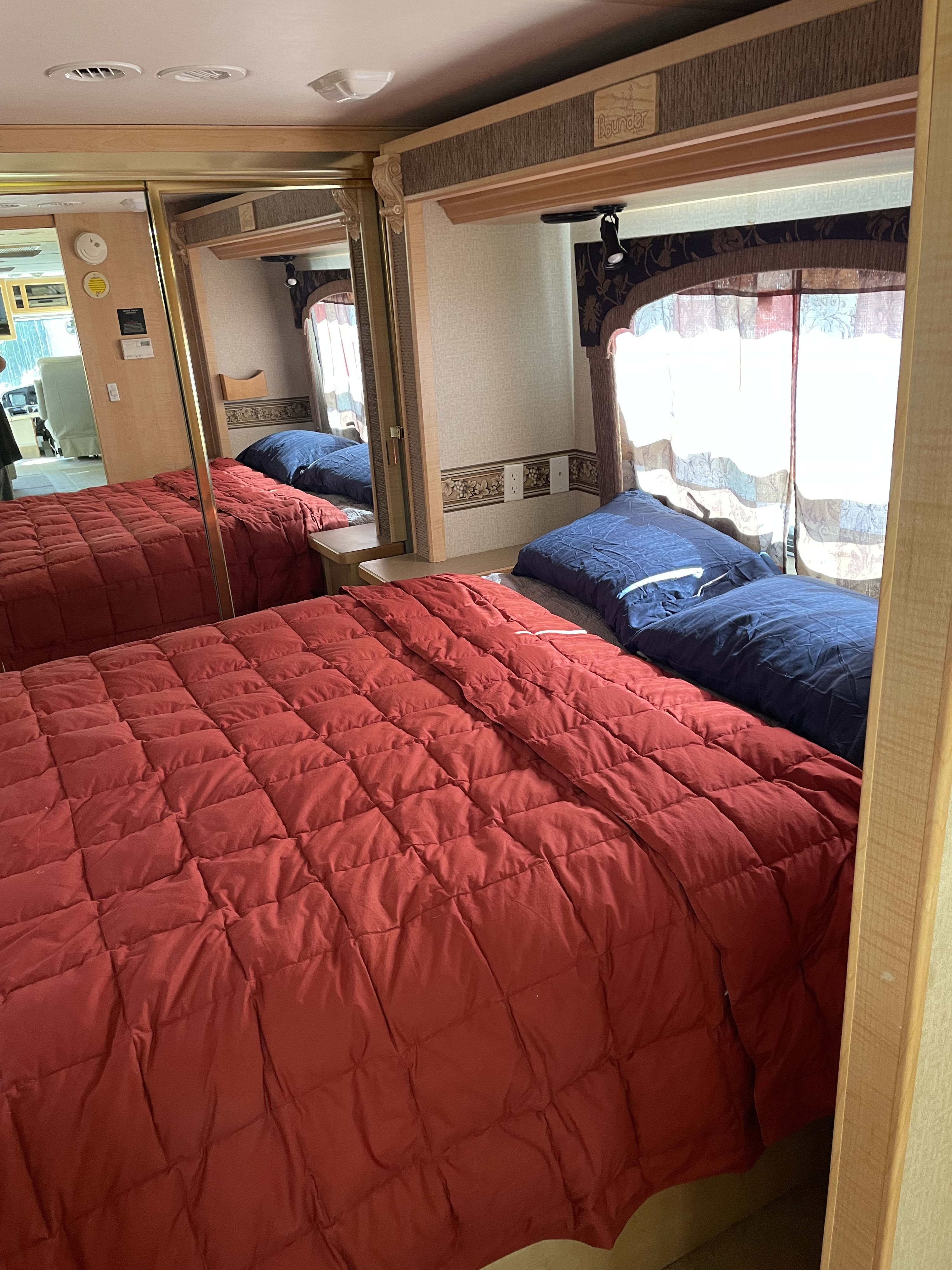 Cozy RV rental bedroom with red comforter, blue pillows, and mirrored closet, brightly lit by windows.. Fleetwood Bounder 37U 2003