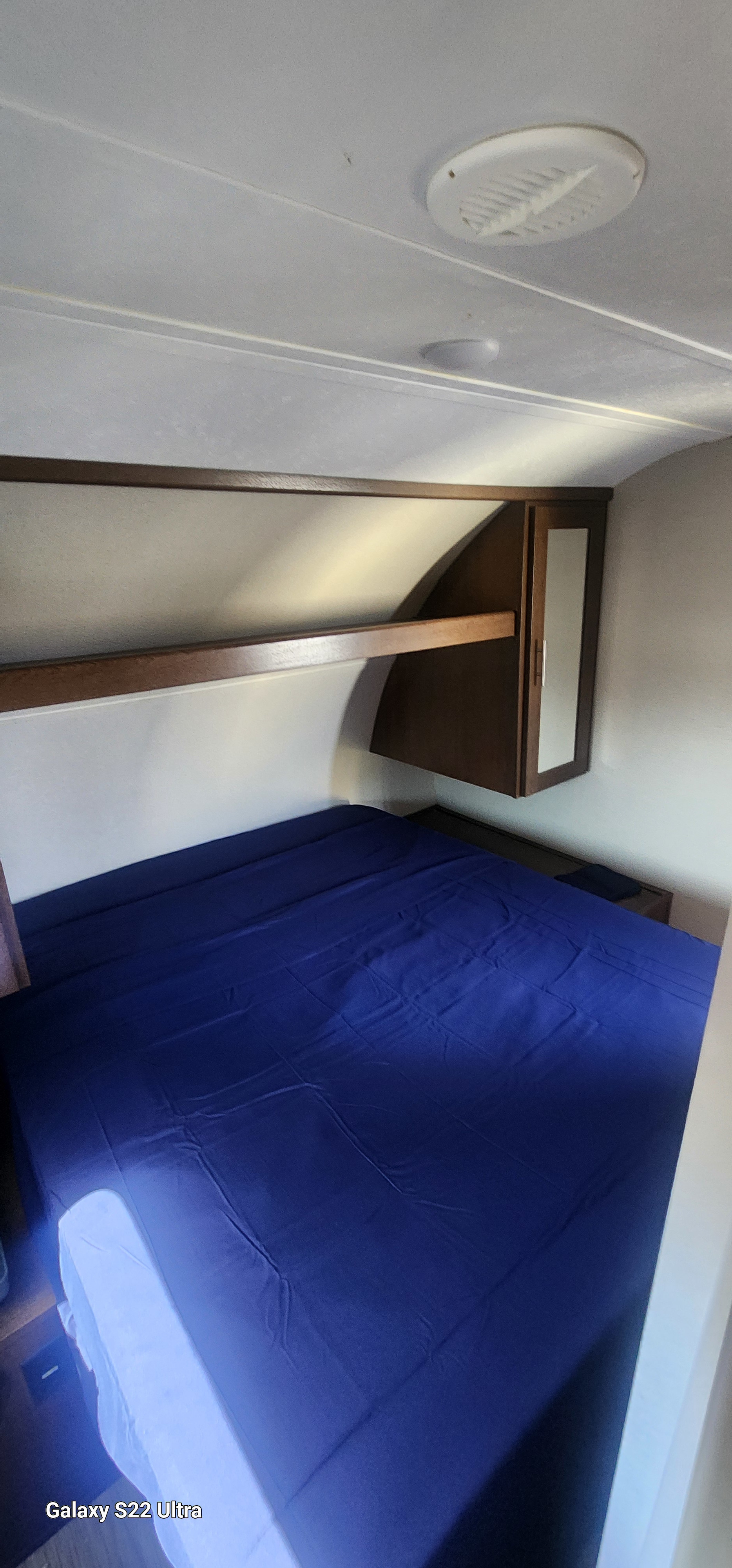 A cozy RV rental bedroom features a blue bed, overhead storage, and cabinet, ideal for travel comfort.. Forest River Tracer Breeze 2019