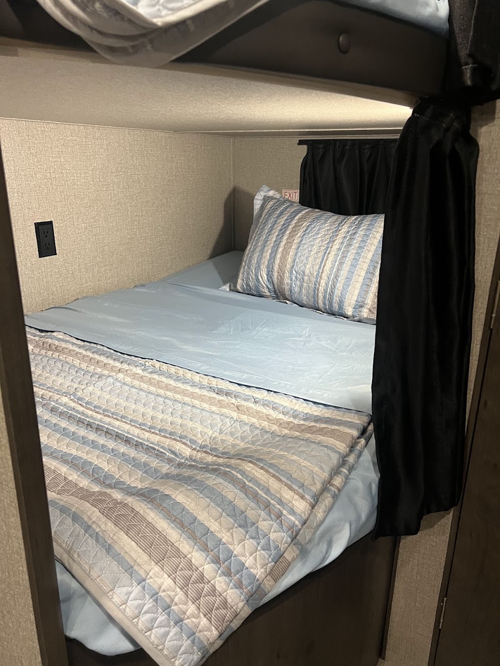 Comfortable RV rental bunk bed with blue sheets, striped quilt, pillow, power outlet, and privacy curtain.. Jayco JayFlight 2021