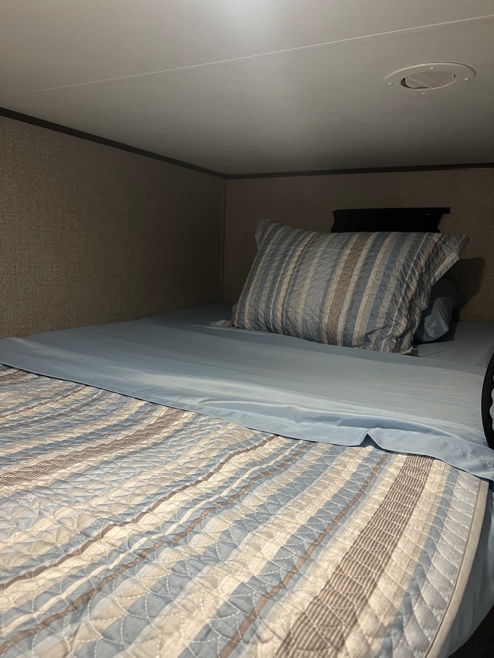 Cozy bunk bed in an RV rental, featuring soft blue sheets and a striped quilt. Ideal for comfortable travel lodging.. Jayco JayFlight 2021