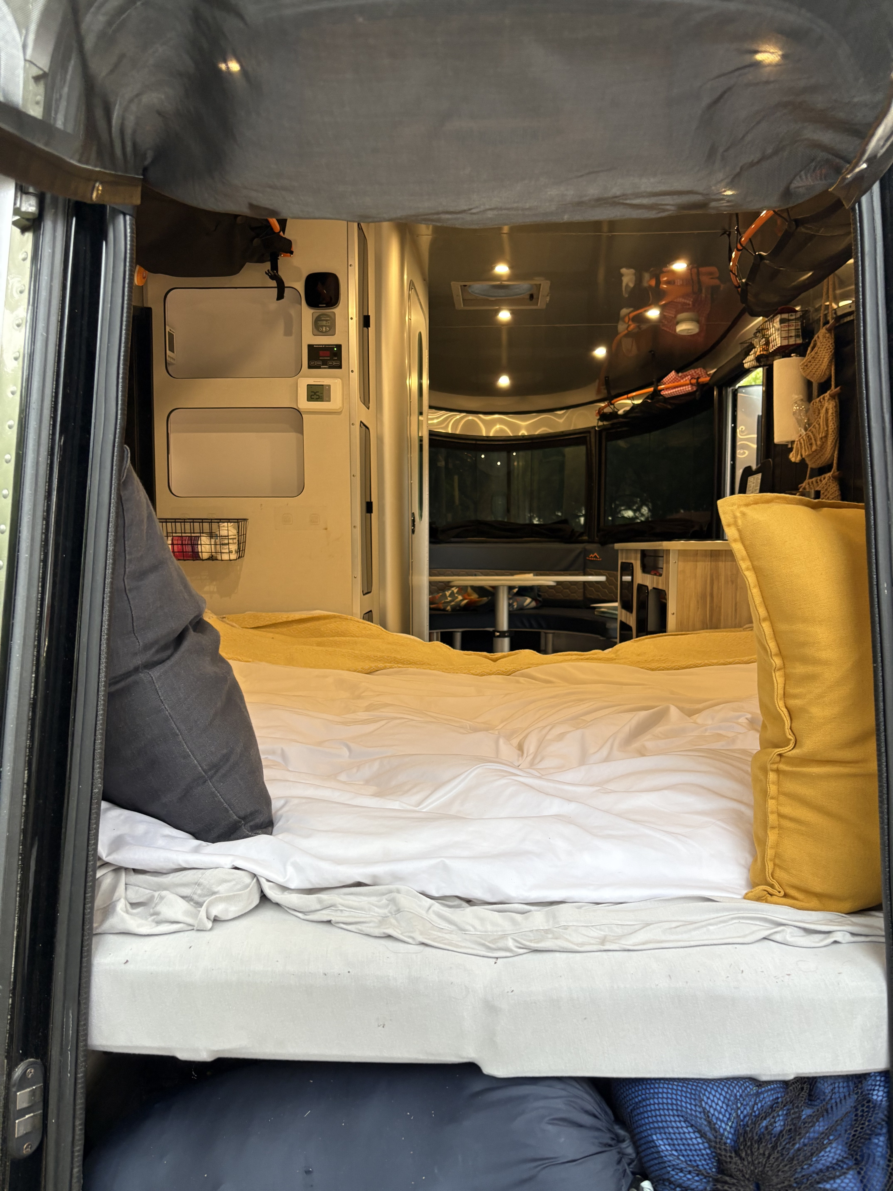 Comfortable RV rental bed provides a view of the modern interior with kitchen, dining, and controls.. Airstream Basecamp 2023