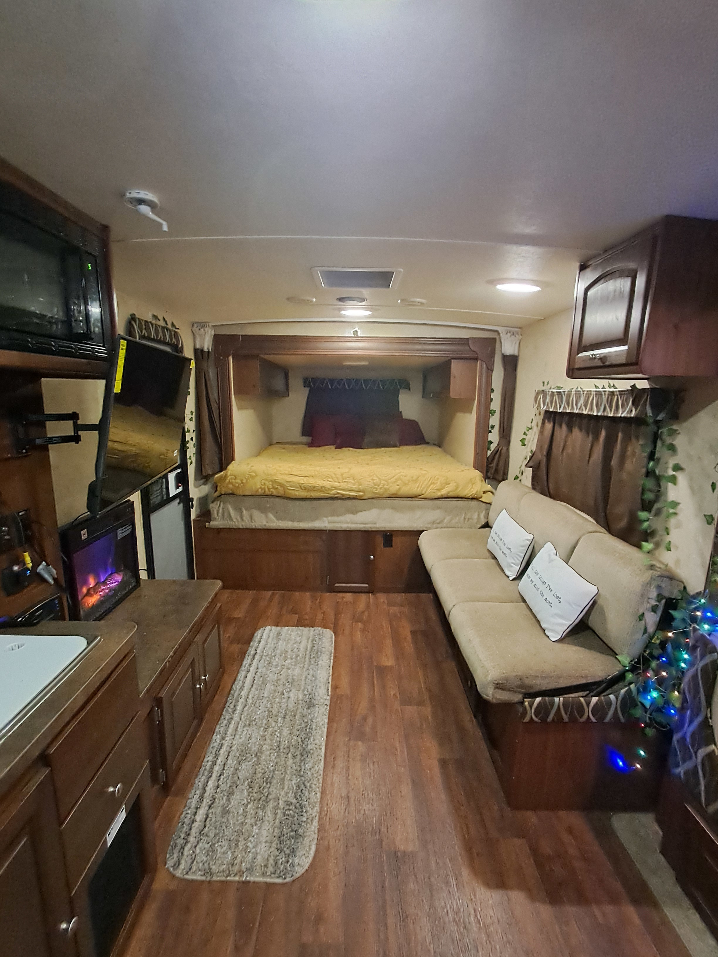Inside an RV rental: full bed at rear, cozy couch right, kitchen/TV left. Wood floors and string lights add warmth.. Forest River Flagstaff Shamrock 2014