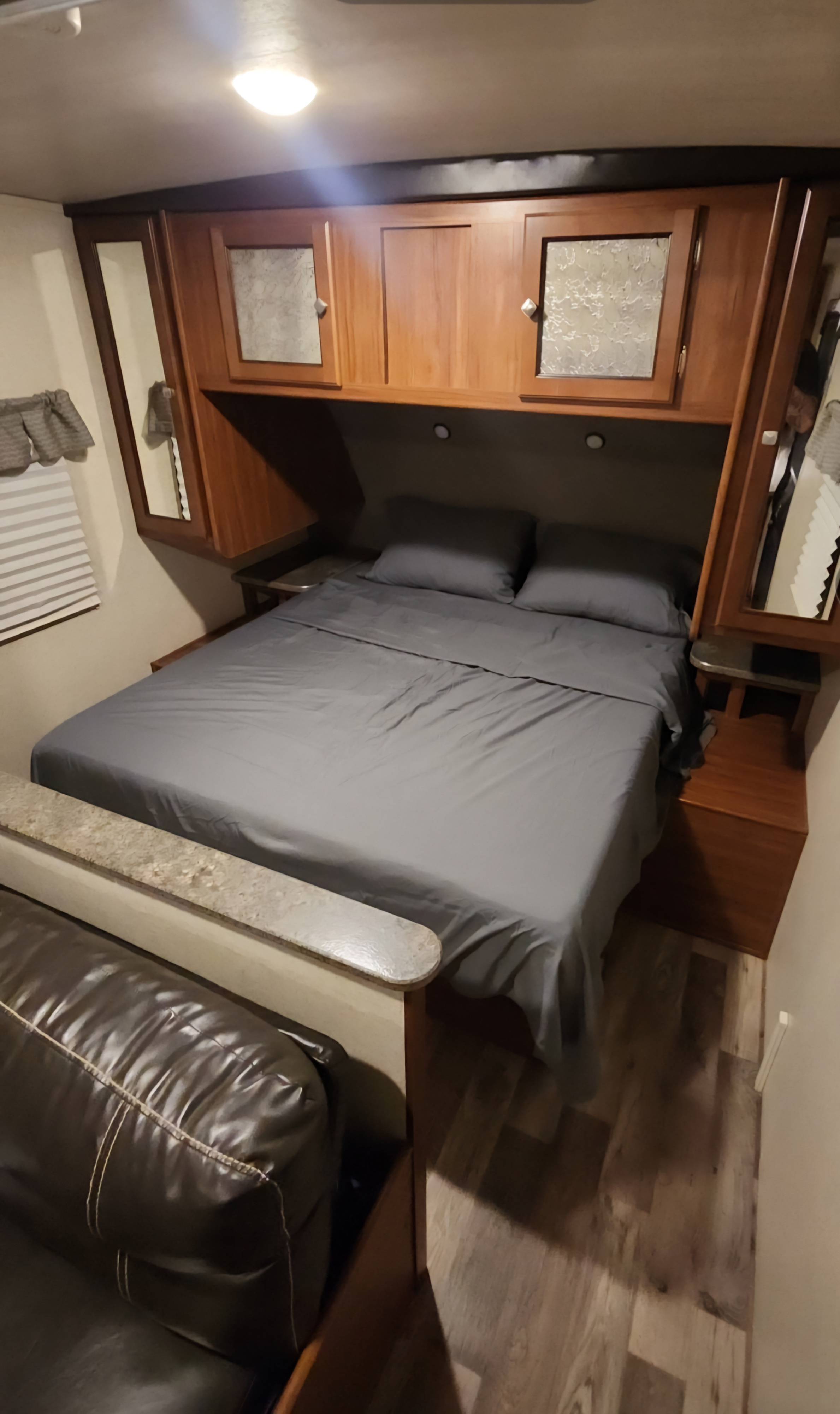 Cozy RV rental bedroom featuring a grey bed, wooden cabinets, and a brown leather couch for a comfortable stay.. Heartland RVs Wilderness 2017
