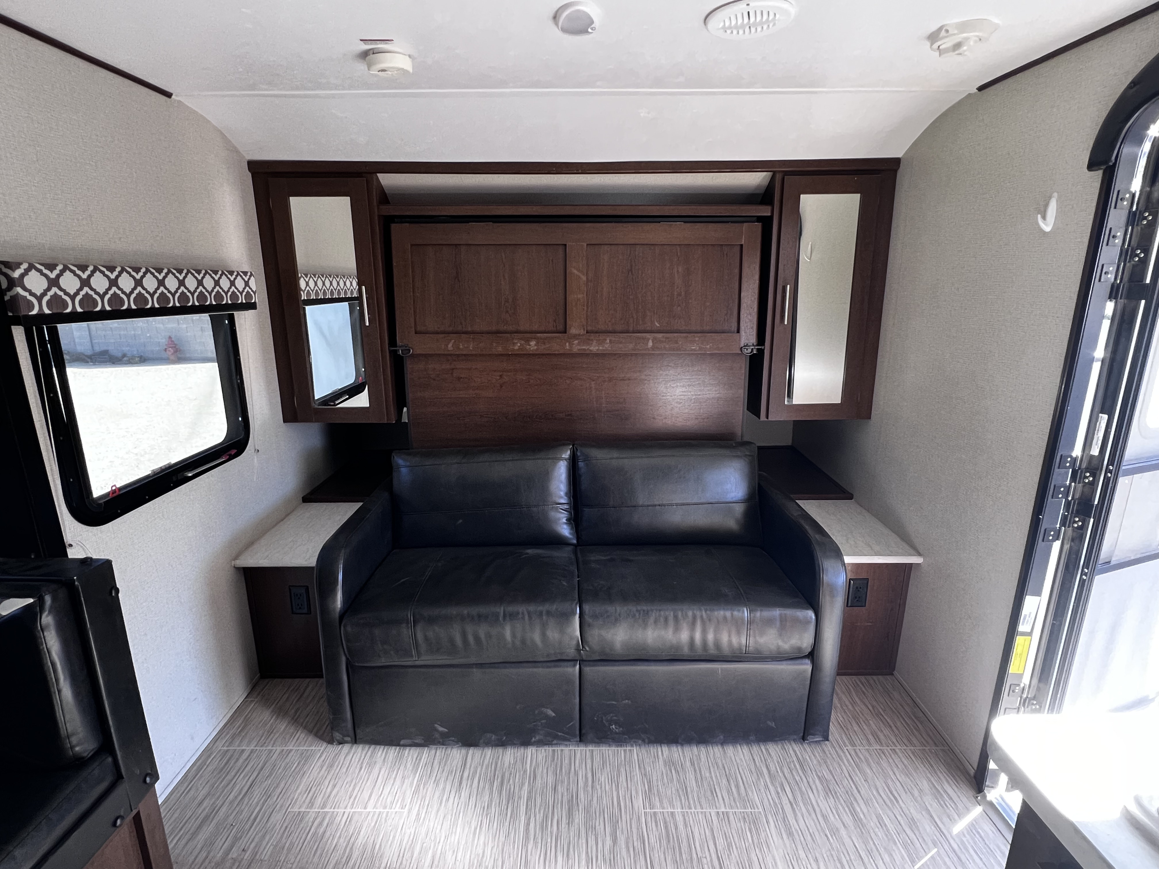 This RV rental features a cozy living space with a black sofa, convertible murphy bed, and built-in storage.. Forest River Tracer Breeze 2018