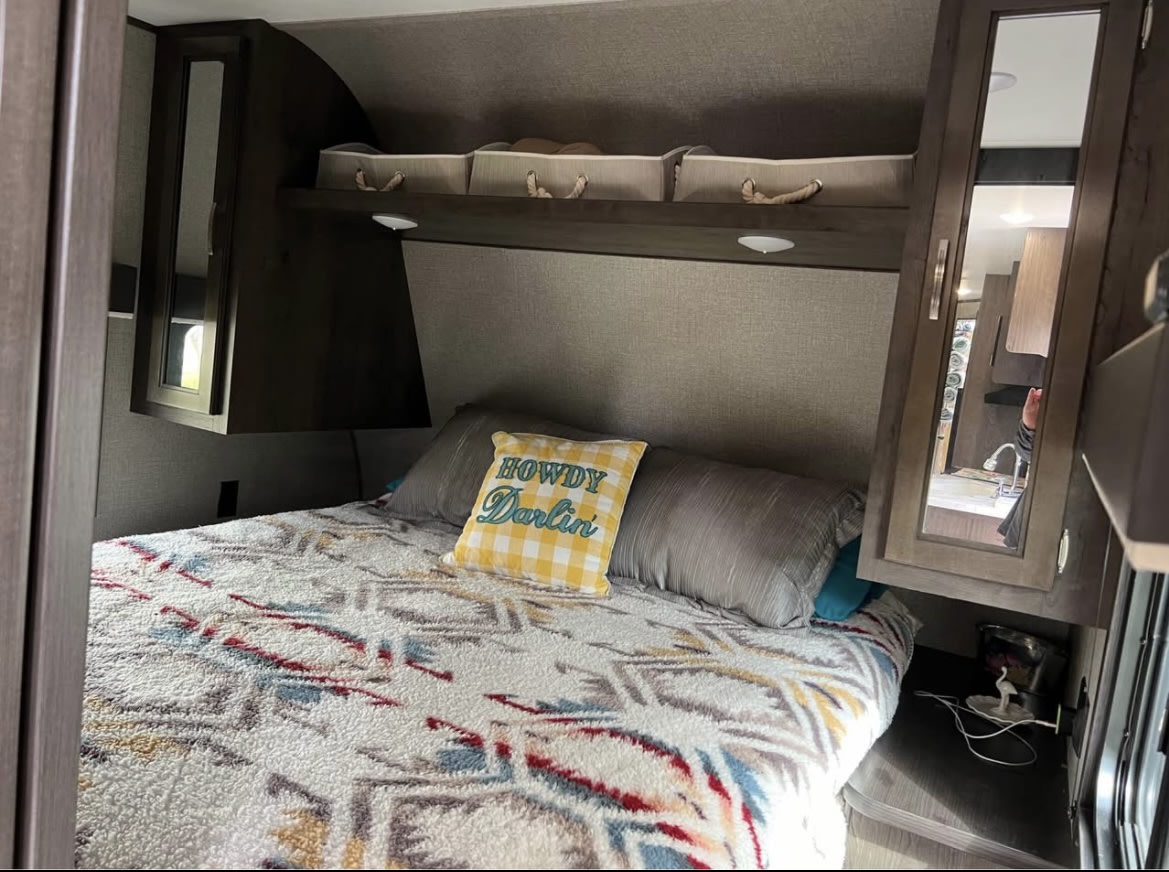 Cozy RV rental bedroom features a patterned bed, 'Howdy Darlin'' pillow, overhead storage, and mirrored cabinets.. Jayco Jay Flight SLX 2021