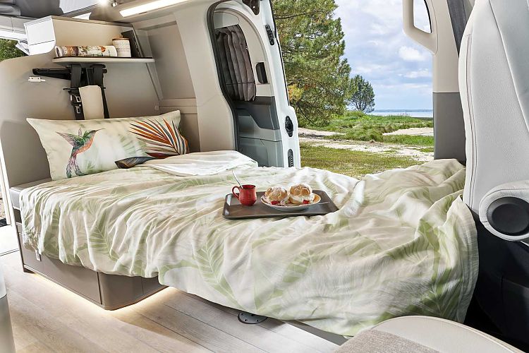 Inside a spacious rv rental: a comfy bed with leafy duvet, hummingbird pillow, and a breakfast tray, overlooking a scenic lake.. Ford Tourneo Long 2025
