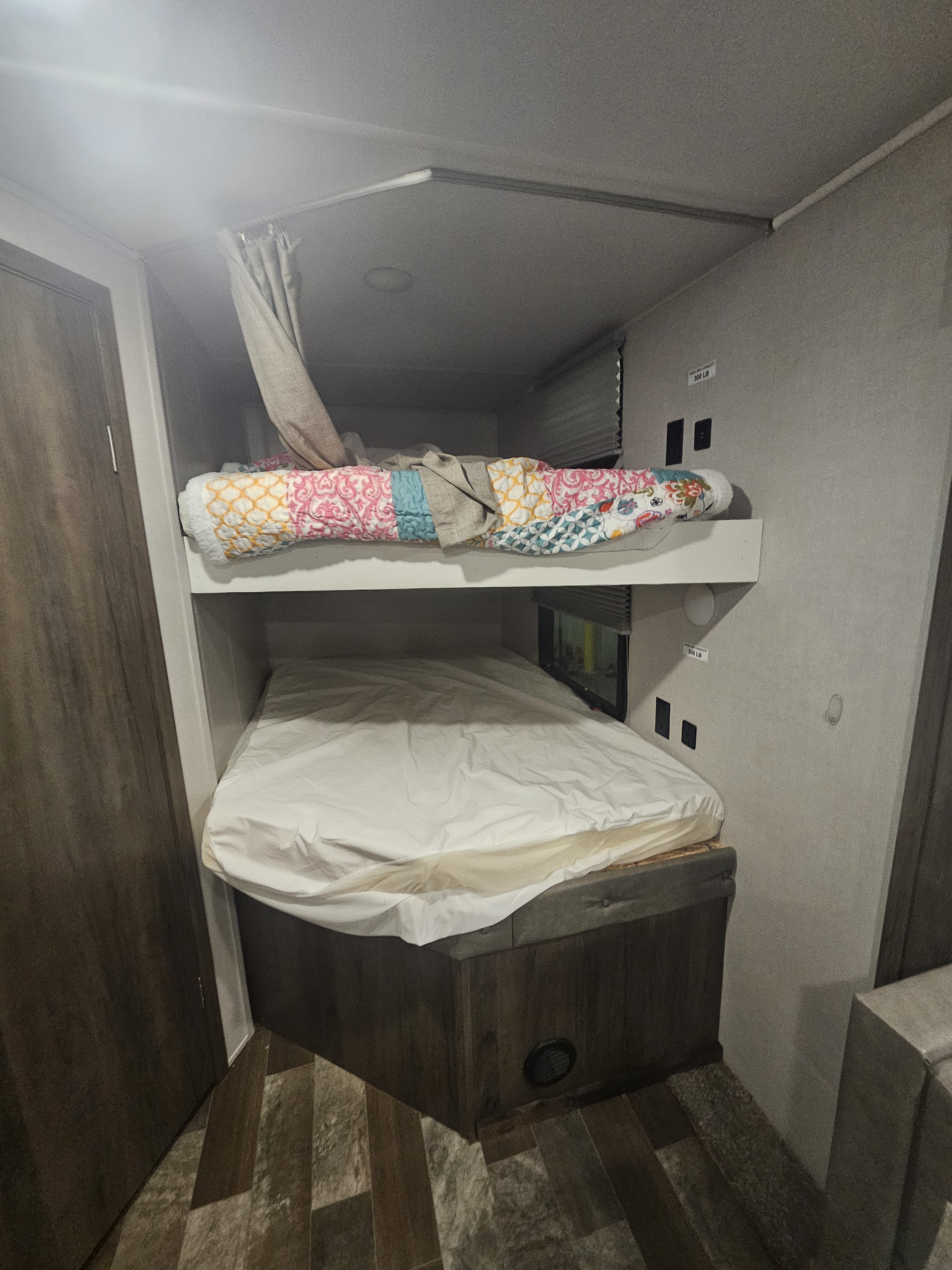 RV rental interior: cozy bunk beds with curtains and outlets, offering comfortable sleeping for family travel in a camper.. Forest River east to west 2020