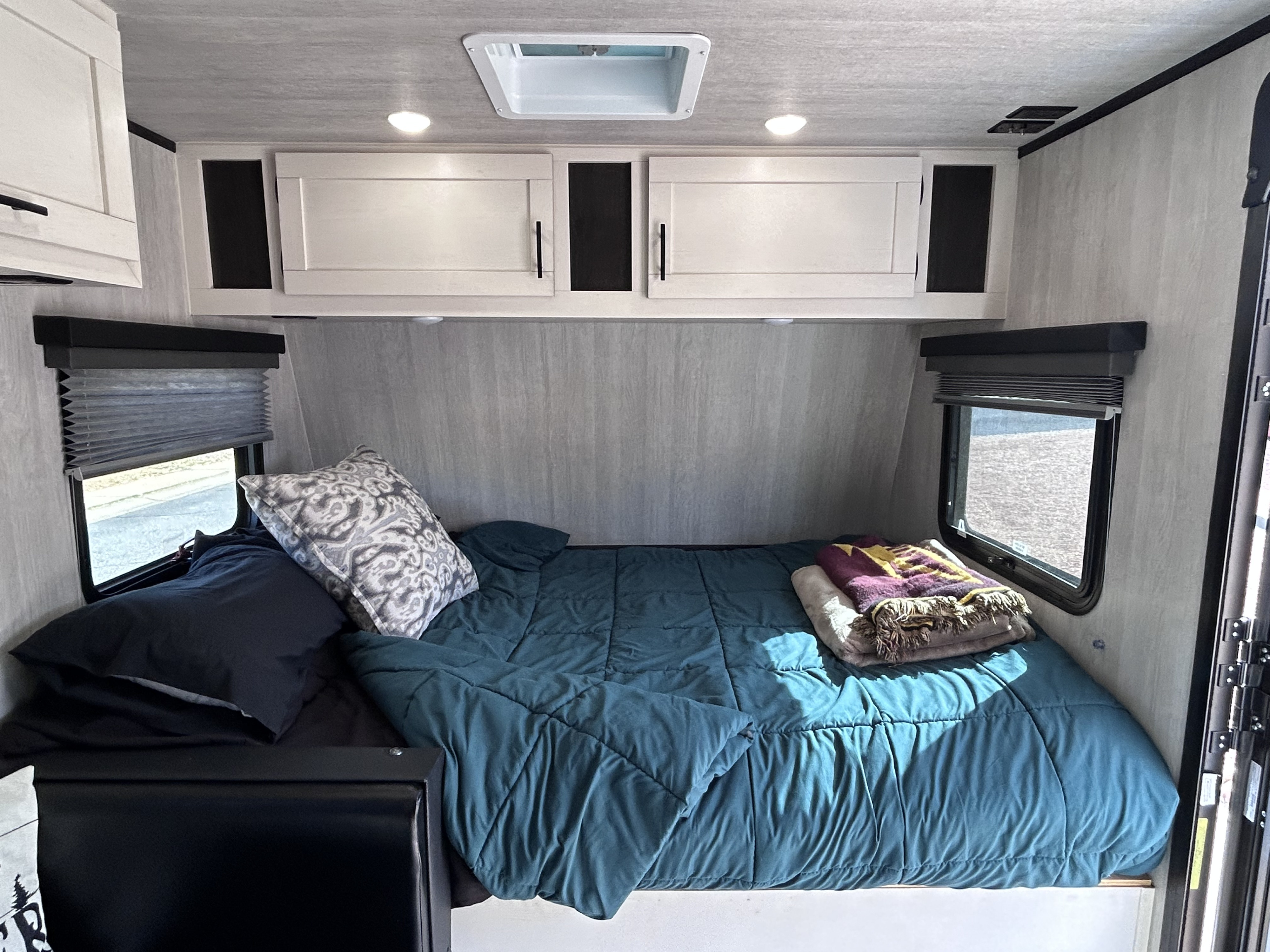 Inside a comfortable RV rental bedroom featuring a teal comforter, crisp white cabinets, and windows with blinds.. Genesis Supreme 16 BB 2024