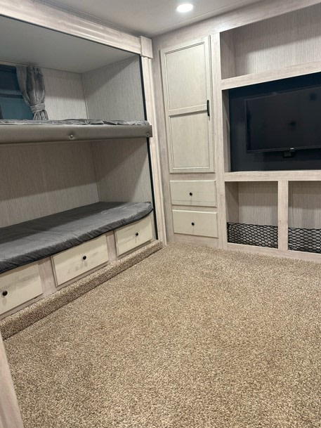 An RV rental interior showcasing bunk beds with storage drawers, a mounted TV, built-in cabinets, and carpeted flooring.. Forest River Sandpiper 2022