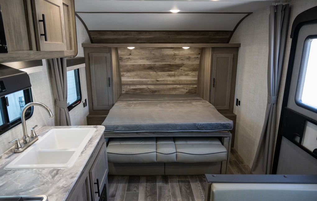 Inside this RV rental, see the cozy sleeping area with a bed, storage, and a kitchen counter with a sink.. Gulf Stream 248BH 2022
