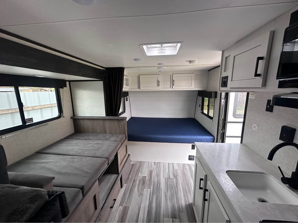 Bright RV rental interior: A bed, convertible bench seating, and a compact kitchen offer a cozy travel space.. Jayco Jay Flight SLX 2024