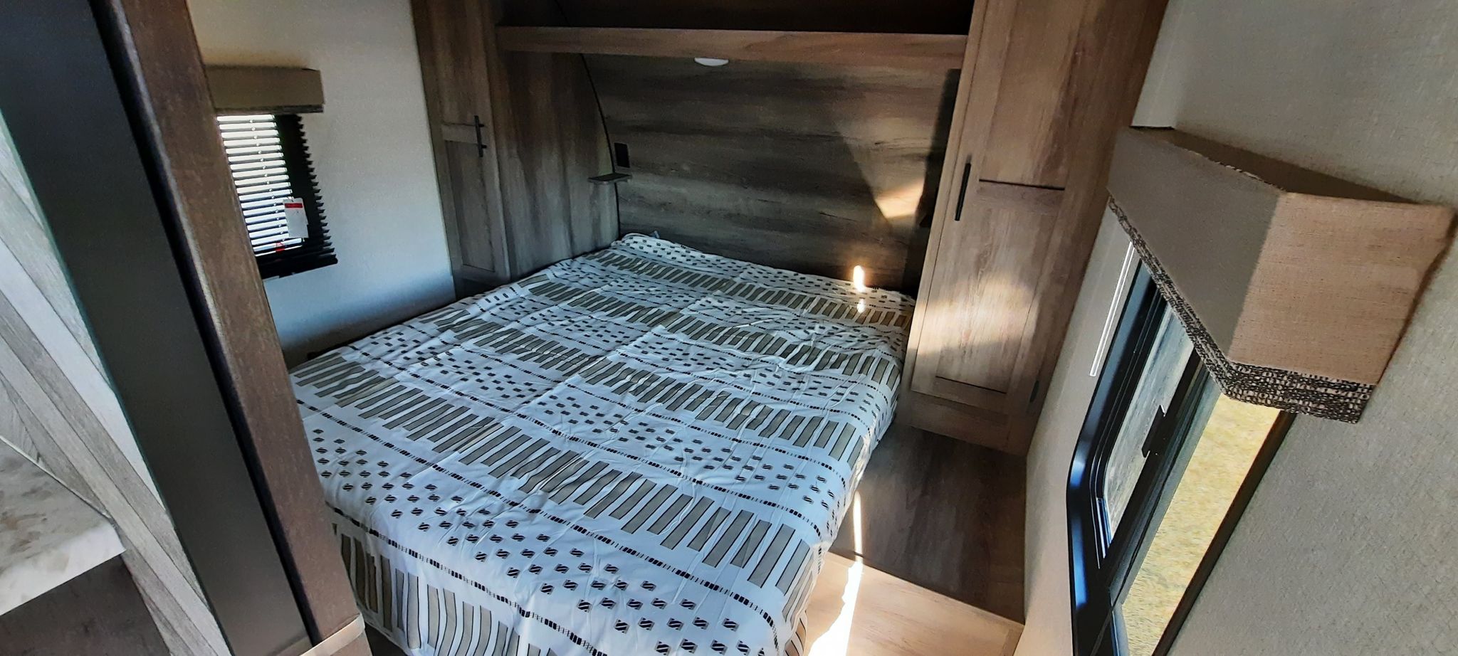 Step inside this inviting RV rental bedroom, complete with a patterned bed, built-in storage, and a sunlit window.. K-Z Manufacturing Sportsmen 301DBSE 2021