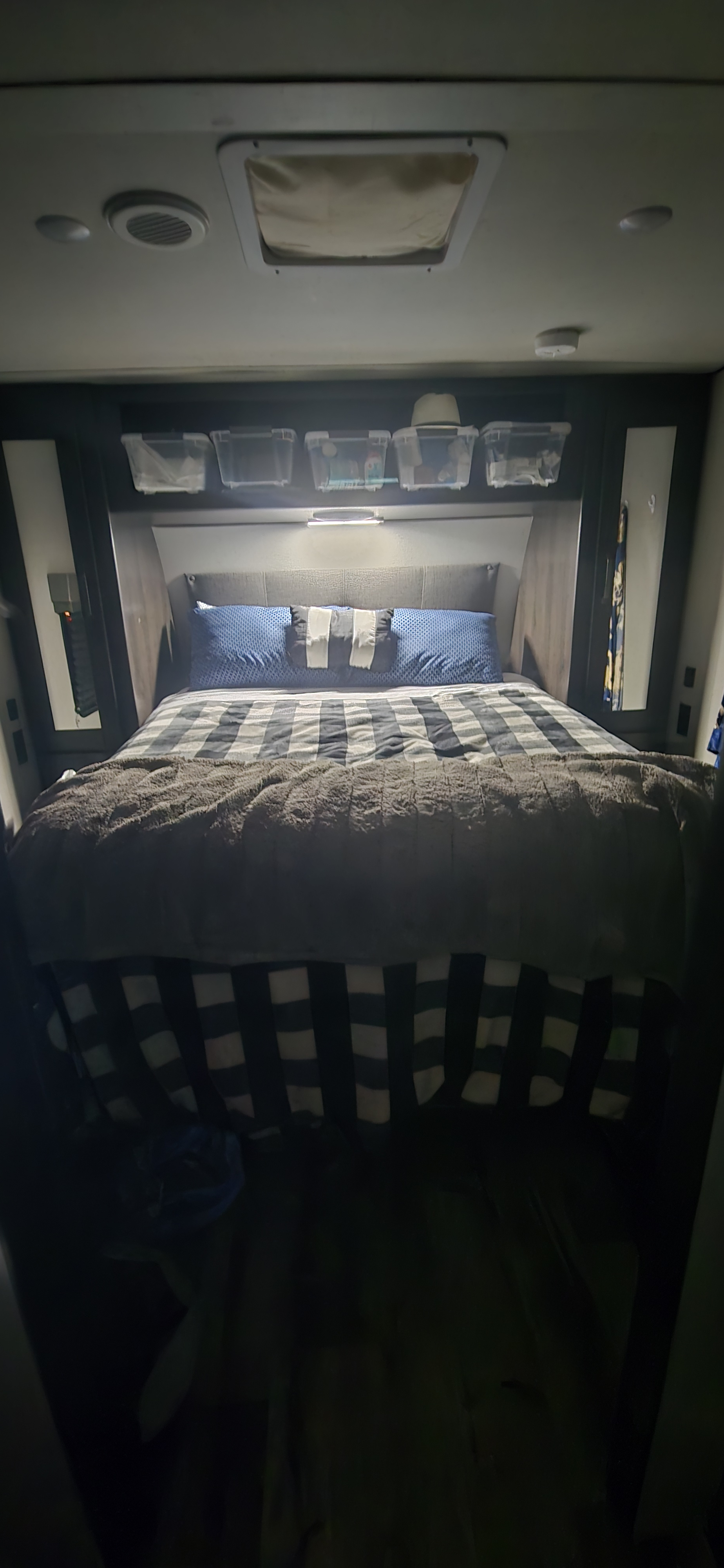 RV rental bedroom: Features a bed with blue and checkered bedding, a fuzzy blanket, overhead storage, and ceiling amenities.. Grand Design Transcend Xplor 2022