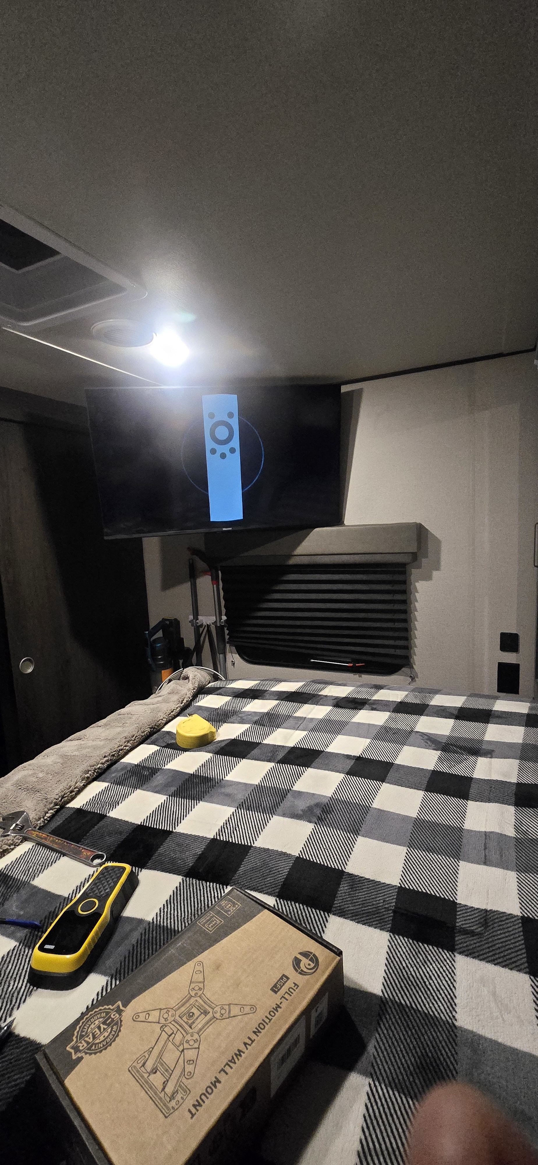 RV rental bedroom: New full-motion TV wall mount box on the plaid bed. TV shows a remote icon, setup in progress.. Grand Design Transcend Xplor 2022