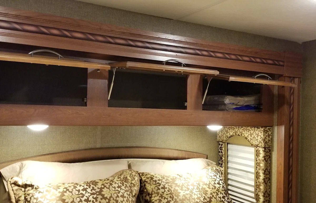 RV rental bedroom showing open wooden overhead cabinets with gas lifts above a cozy bed and ambient lighting.. Thor Motor Coach Freedom Elite 29FE 2017