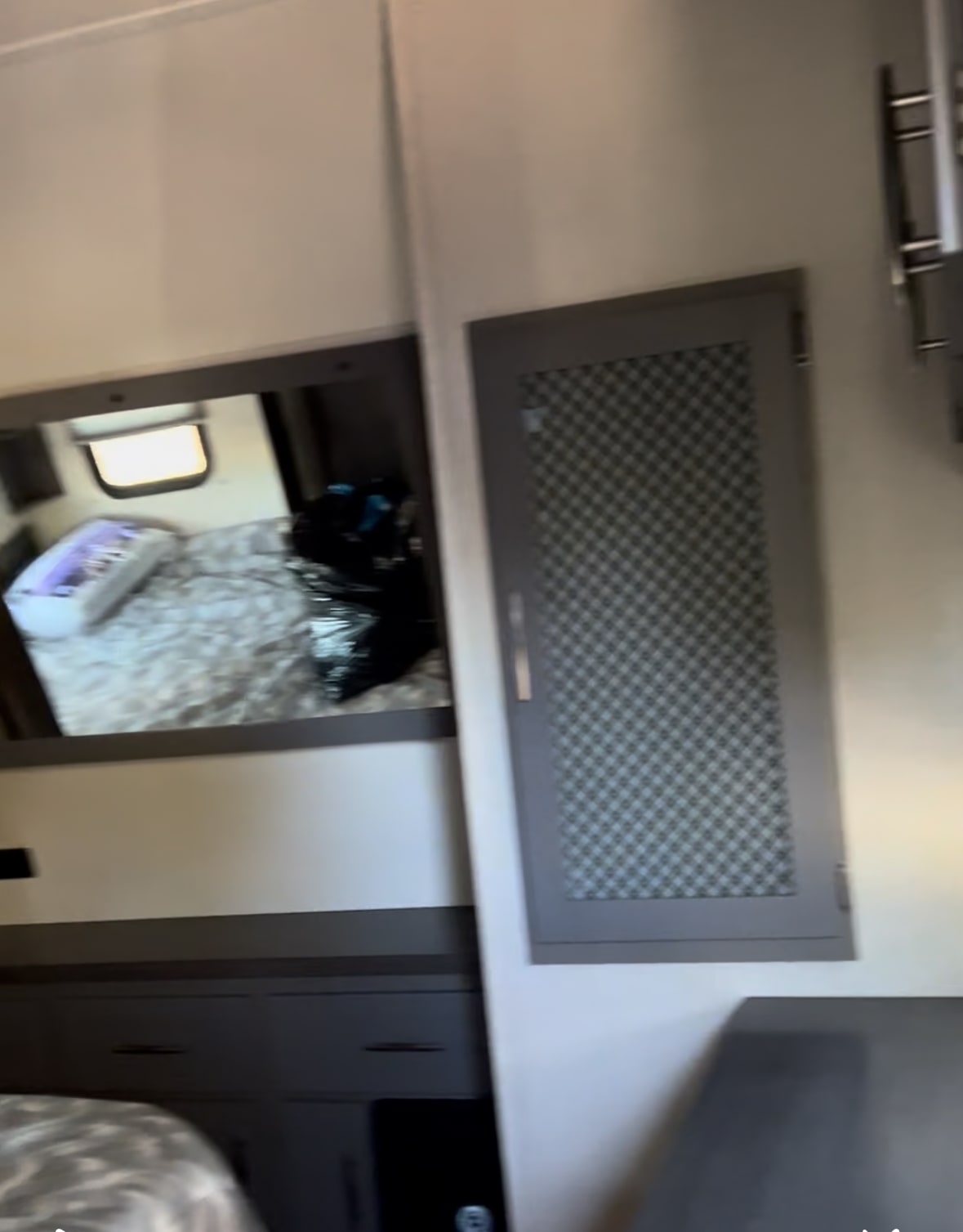 Inside a modern **RV rental**: bedroom area with TV/mirror, dark grey cabinets & storage.. Grand Design Momentum Toy Hauler 2022