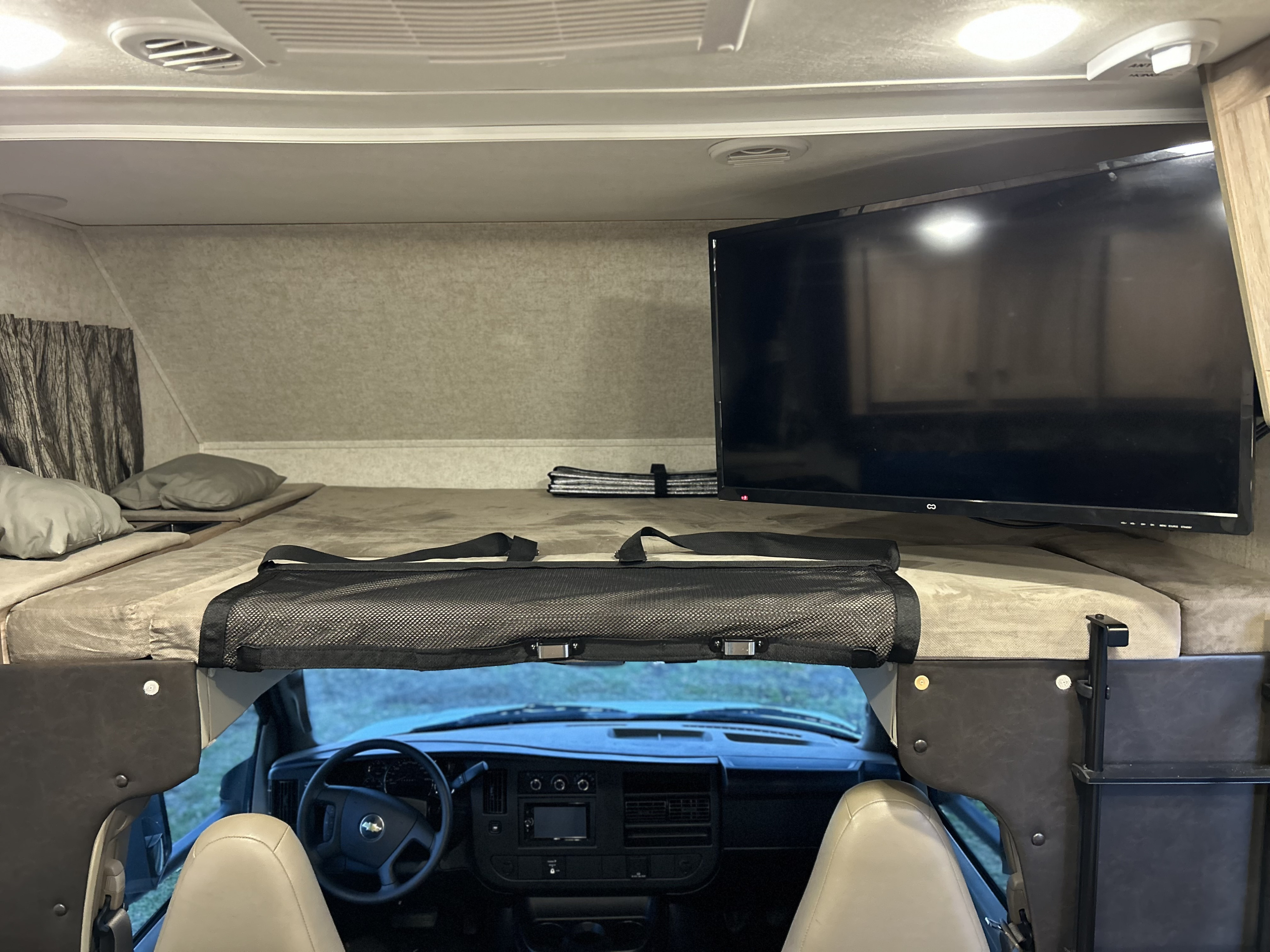Cozy RV rental cab-over bunk bed with TV and safety net, providing a comfortable sleeping area above the vehicle's front cockpit.. Forester Forester Motorhome 2019