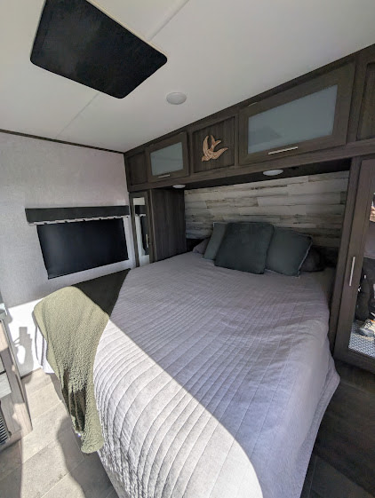 Cozy RV rental bedroom with a large bed, grey comforter, wood headboard, and overhead storage.. Dutchmen Kodiak ultralight 2021