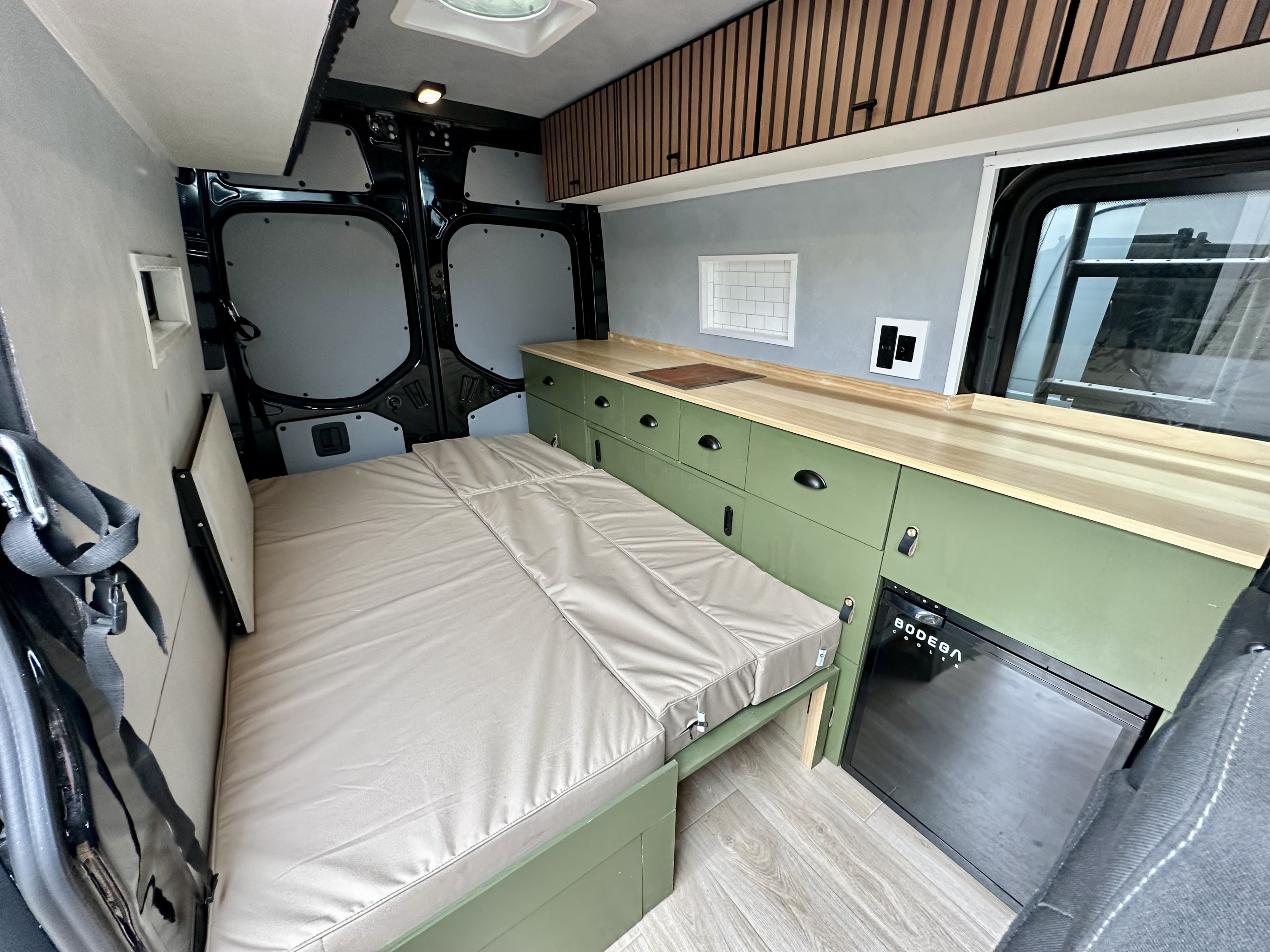 This RV rental interior features a convertible bed, green kitchen with wood counter, fridge, and ample storage.. Mercedes 2500 144" 2019