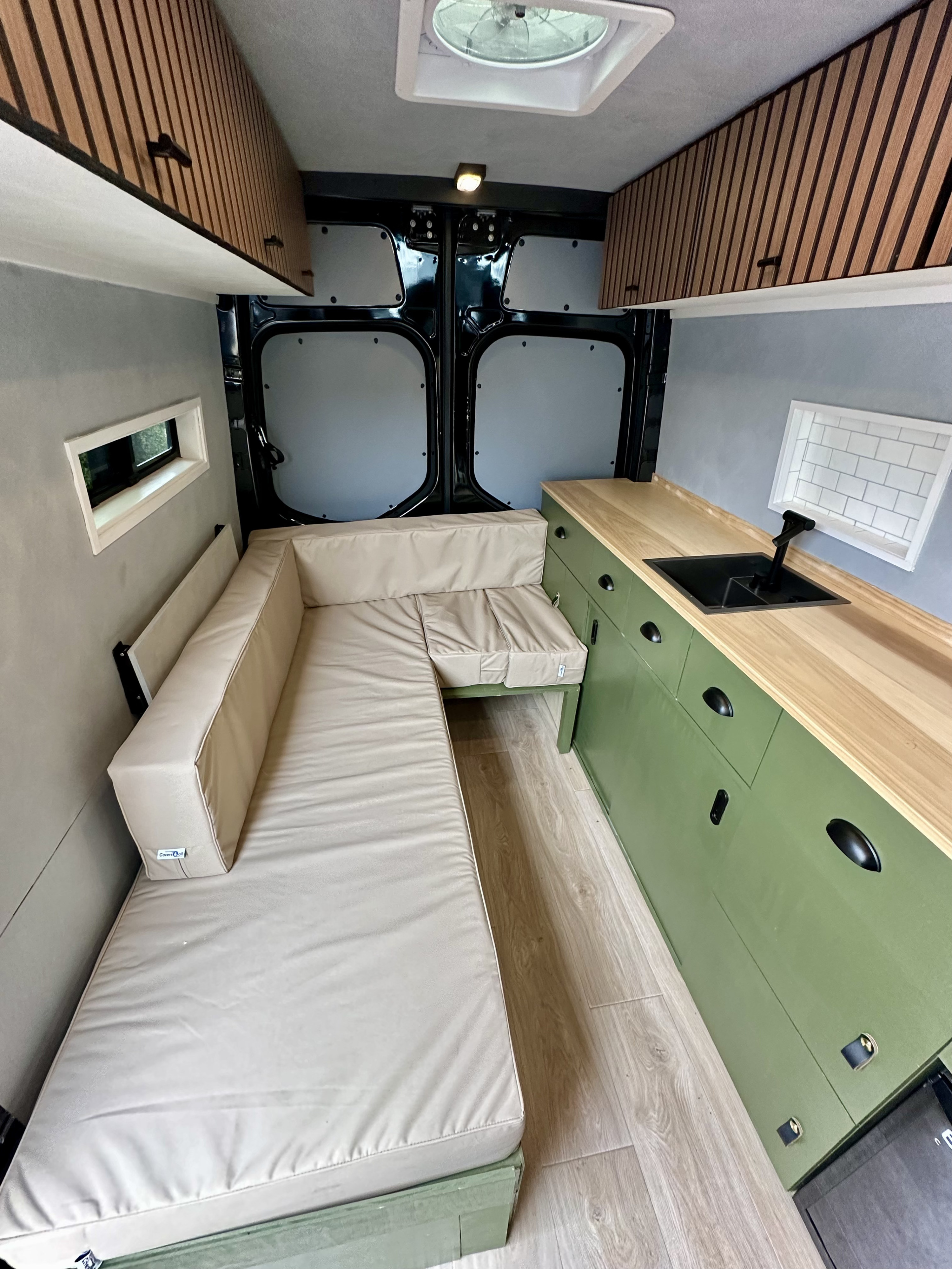 Inside an RV rental camper van: L-shaped bed/seating, green kitchen with wood counter, overhead cabinets.. Mercedes 2500 144" 2019
