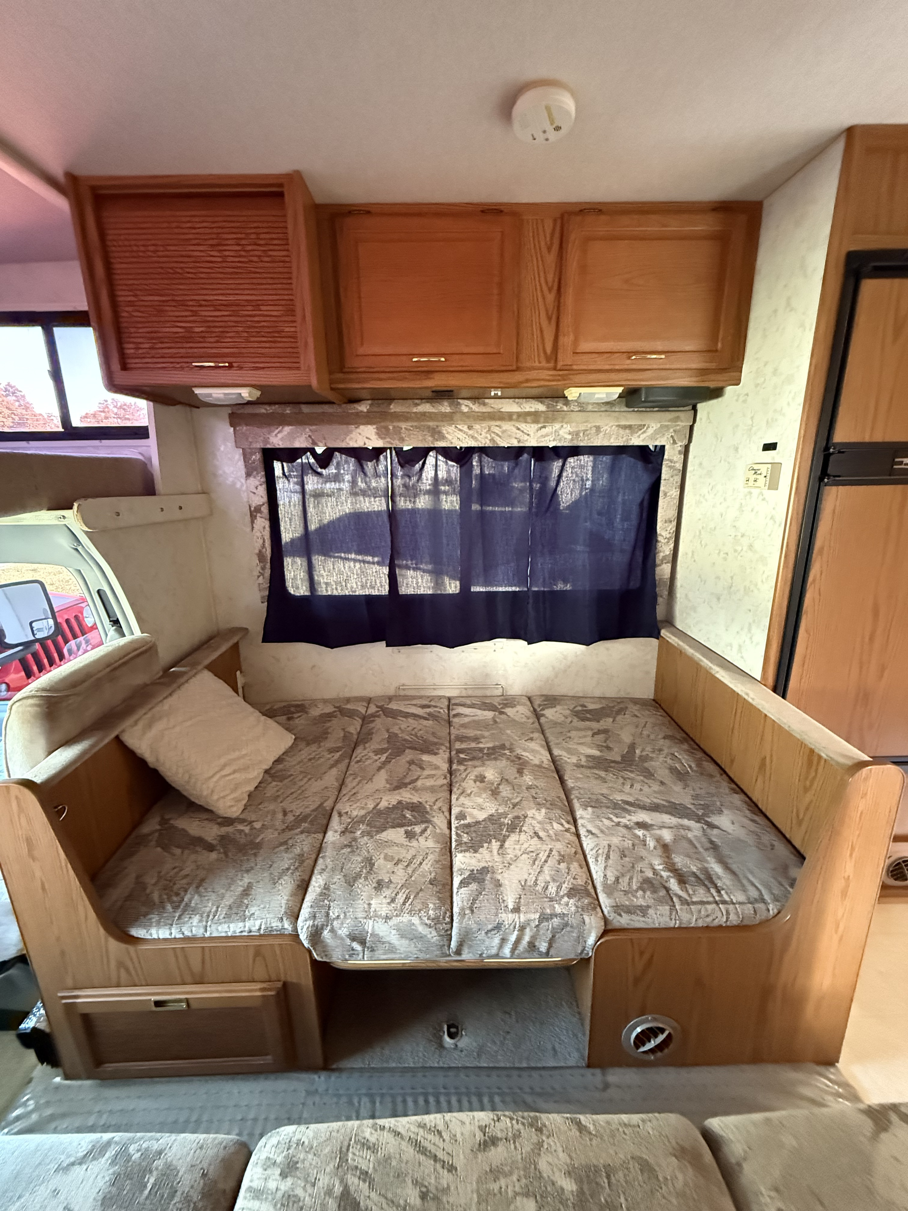 This **RV rental** interior features a cozy, patterned dinette that converts into a bed, with overhead wooden cabinets and windows.. Winnebago Minnie 2000