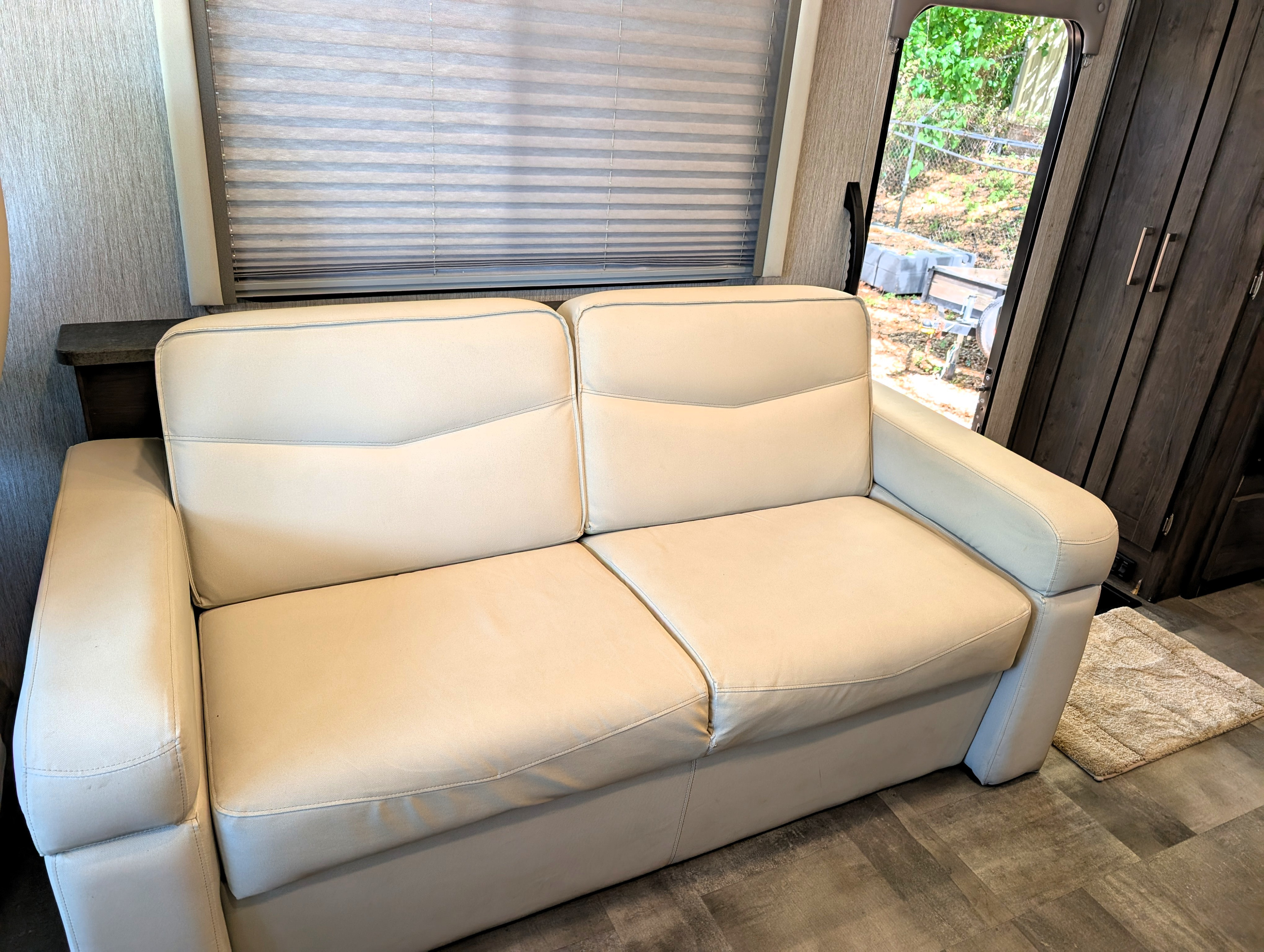 Cozy light-colored sofa in an RV rental interior, complete with blinds and wood accents.. Coachmen Pursuit 2022
