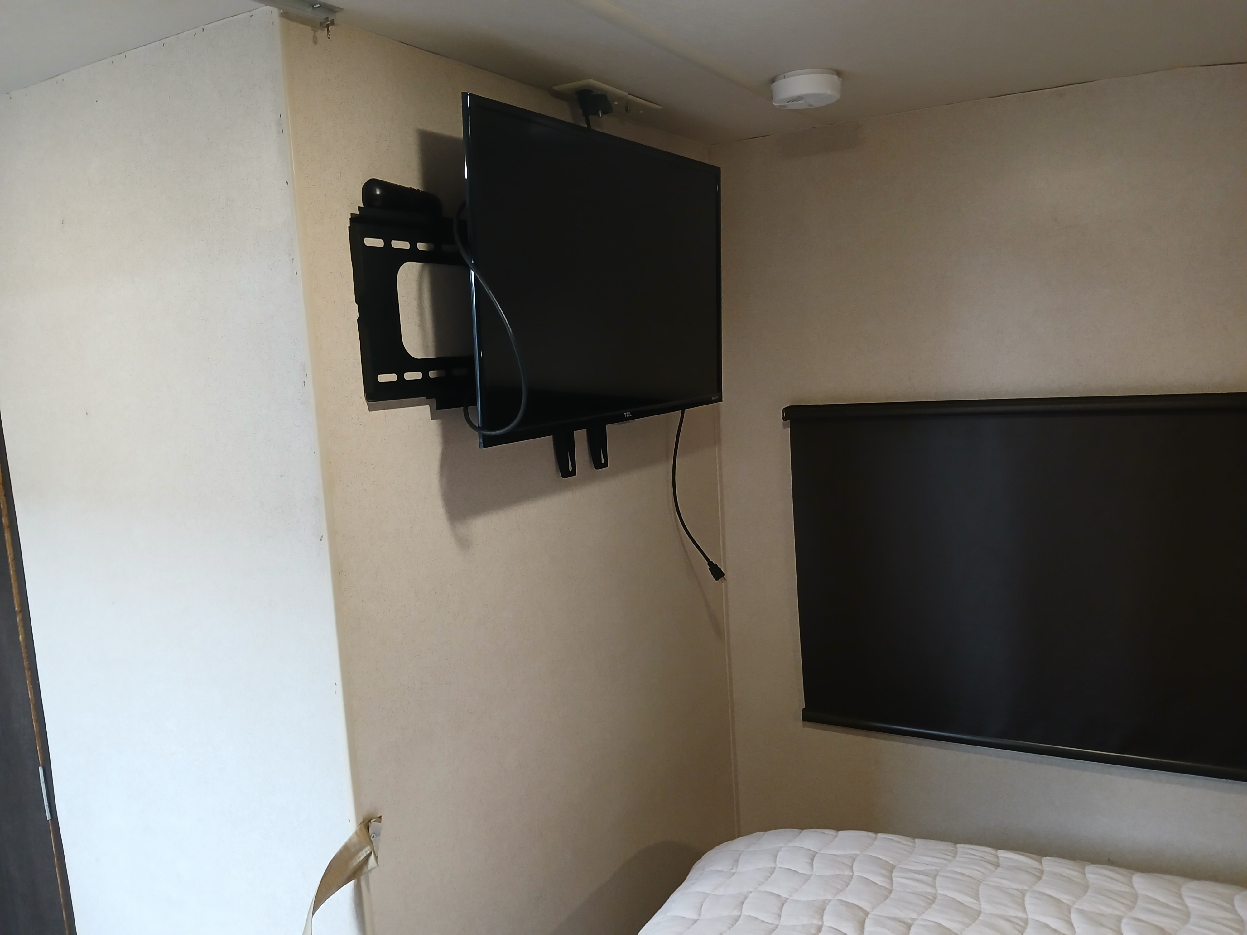 RV rental interior features: wall-mounted TV, ceiling smoke detector, black roller blind, and quilted bed.. Forest River Salem Cruise Lite 2018