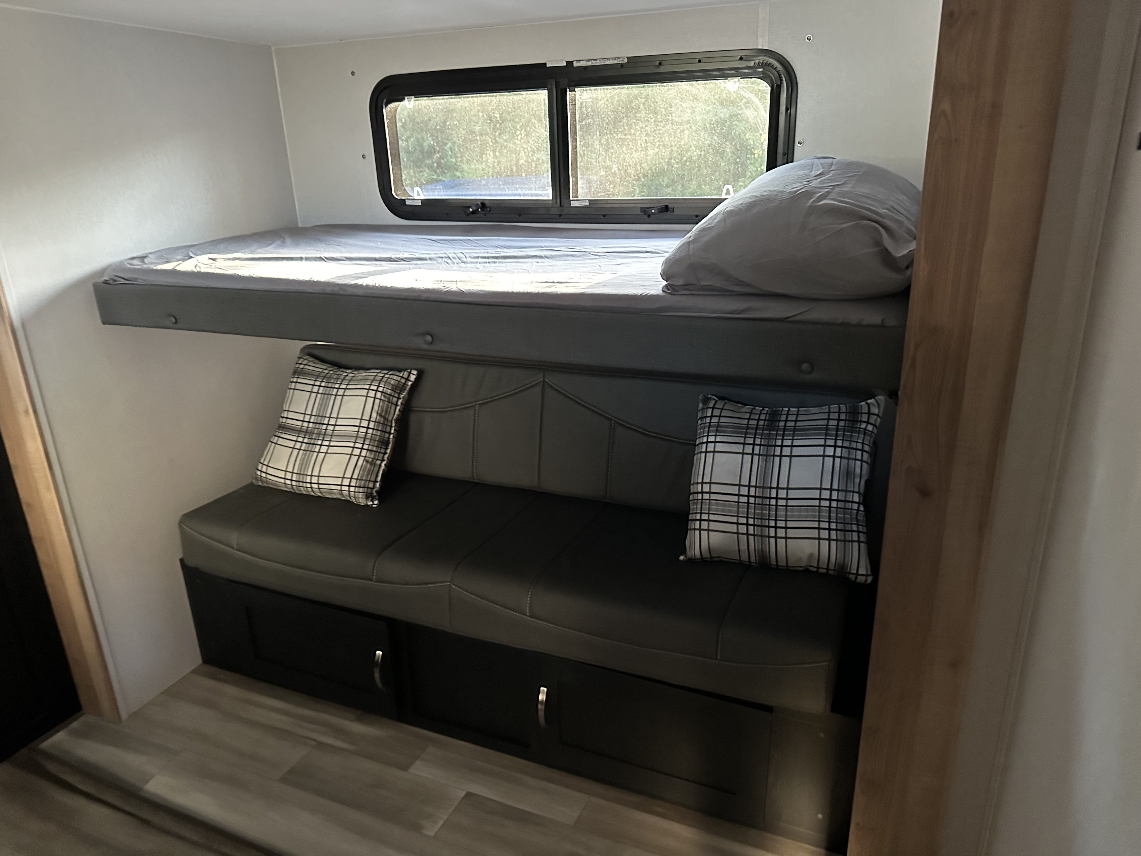 RV rental interior: A top bunk bed, a lower sofa that converts to a bed, and storage drawers. Natural light from a window.. Coachmen 320BHDSLE 2023