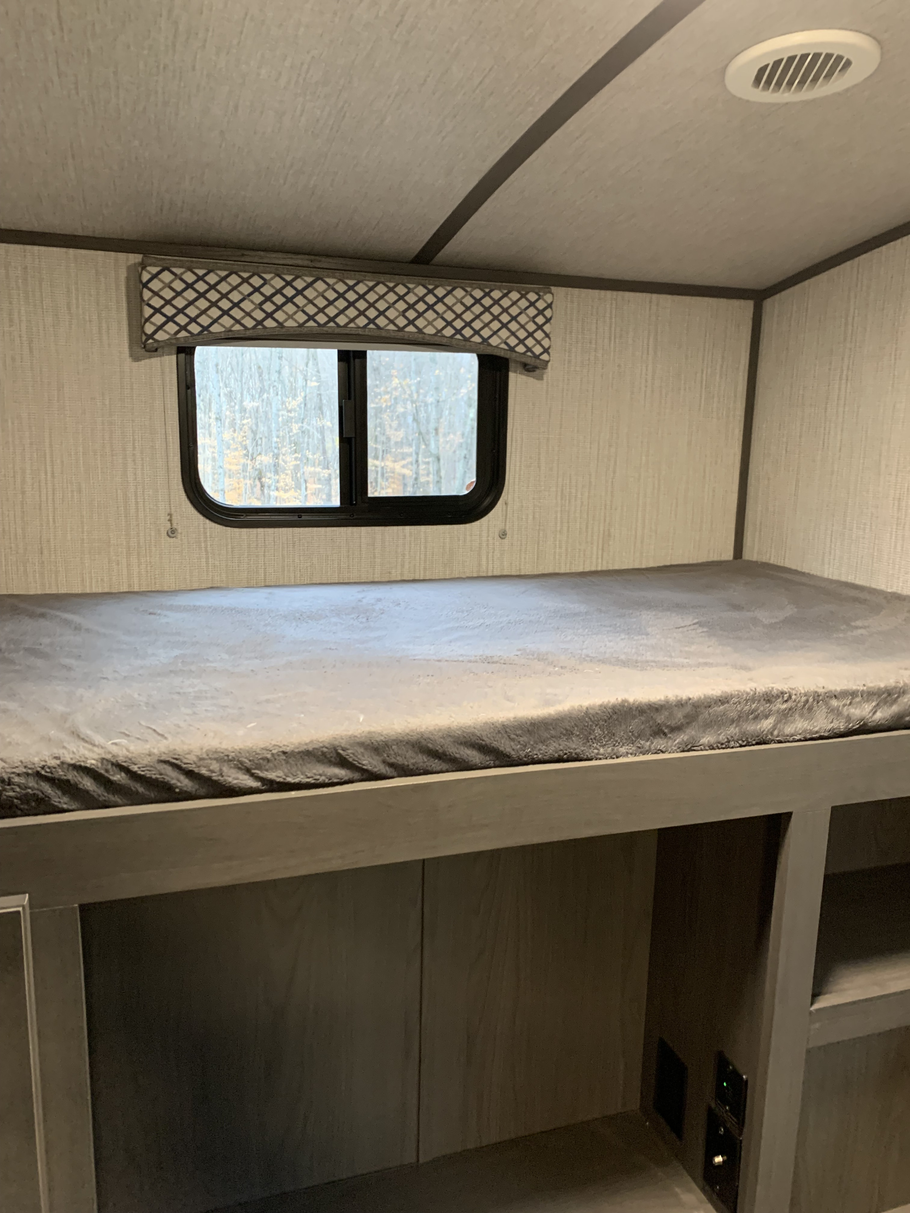 RV rental bunk bed featuring a cozy gray blanket, window with nature view, light-toned interior walls, and built-in storage below.. Cruiser Rv Corp embrace el 310 2020