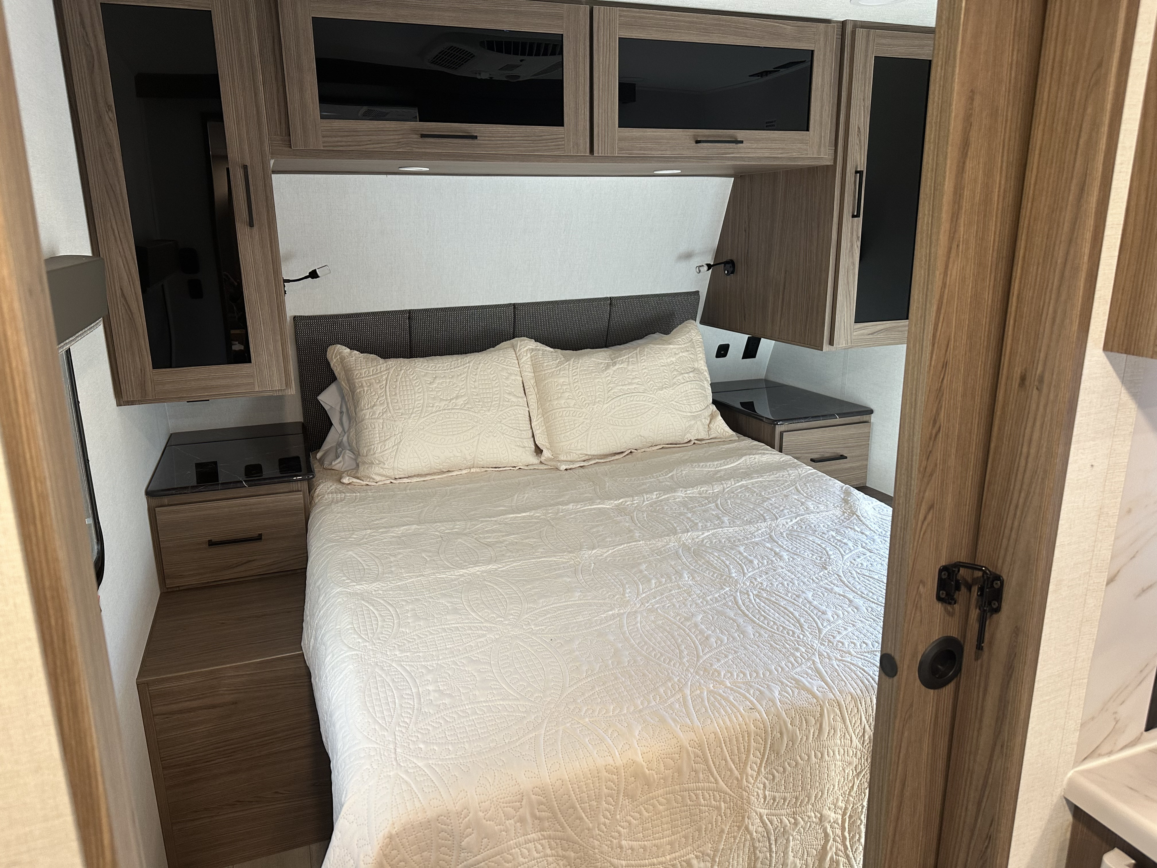 Inviting RV rental bedroom features a comfy bed, overhead cabinets, and practical nightstands for your travels.. Alliance RV Delta 251BH 2024