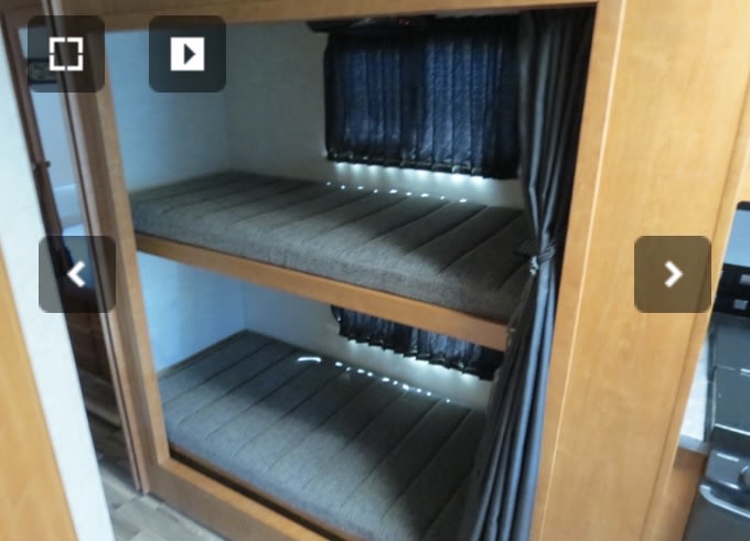 RV rental interior with two bunk beds, complete with grey mattresses, dark privacy curtains, and glowing LED accent lights.. Winnebago Sunstar 2018