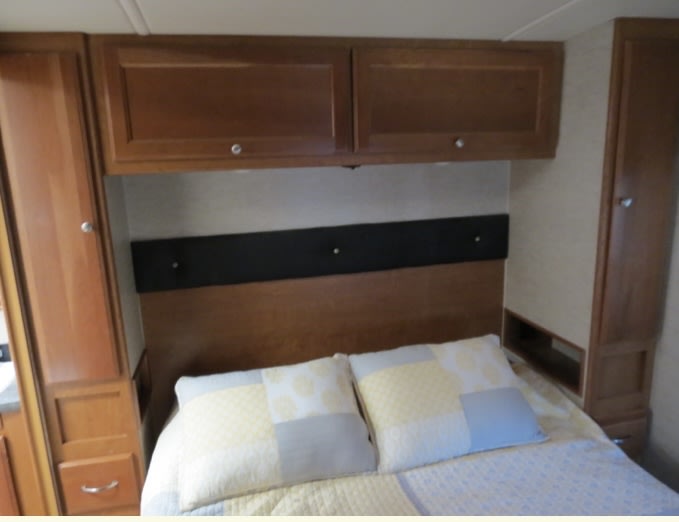 Cozy RV rental bedroom showing a bed, overhead cabinets, and built-in side storage for efficient use of space.. Winnebago Sunstar 2018