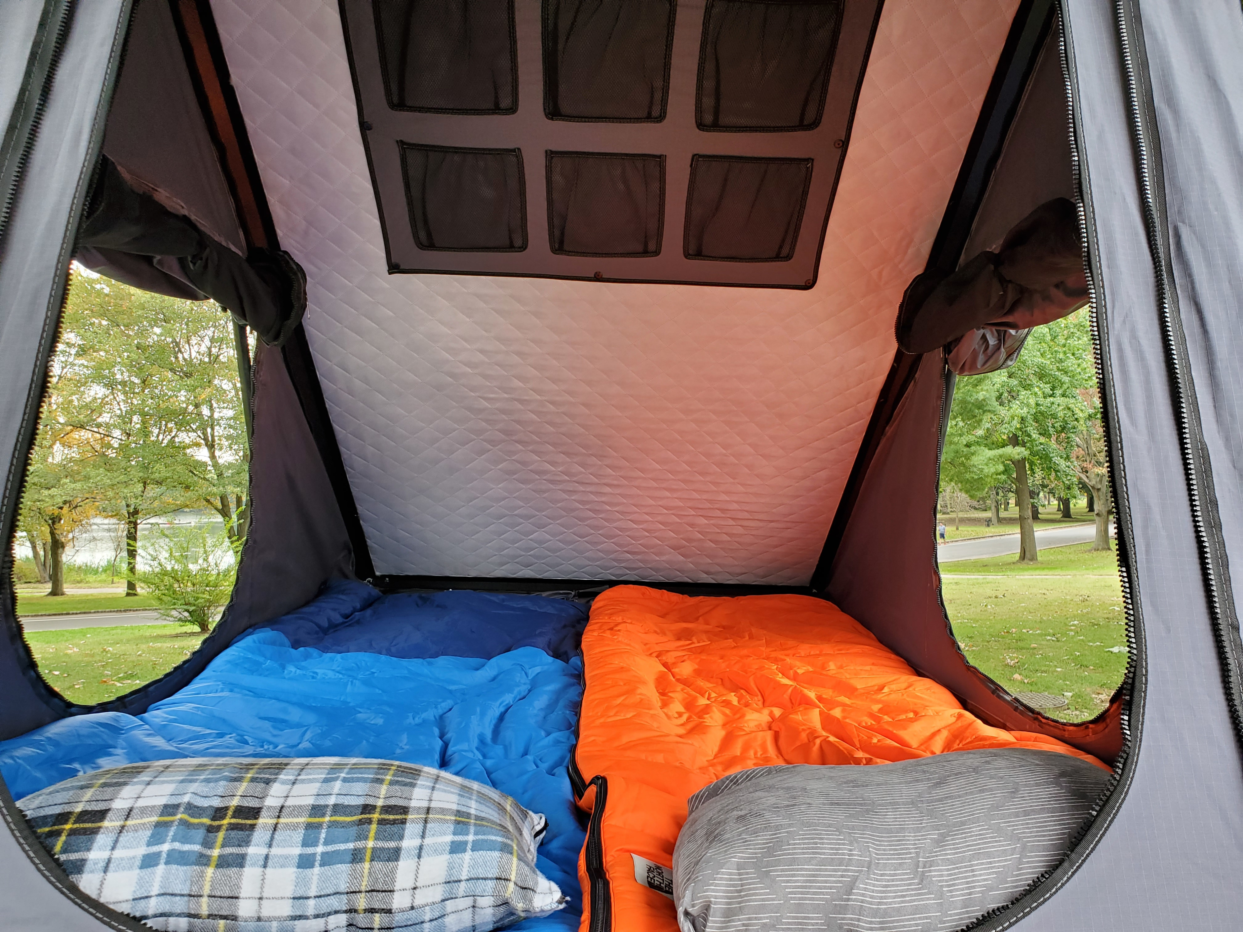 Inside a cozy RV rental: two sleeping bags and pillows, with a panoramic view of a park and lake.. Nissan XTerra 2012