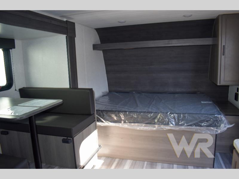 Inside an RV rental: a compact dinette booth and new bed with plastic wrap. Ready for travel.. Keystone RV Hideout Sport 2024