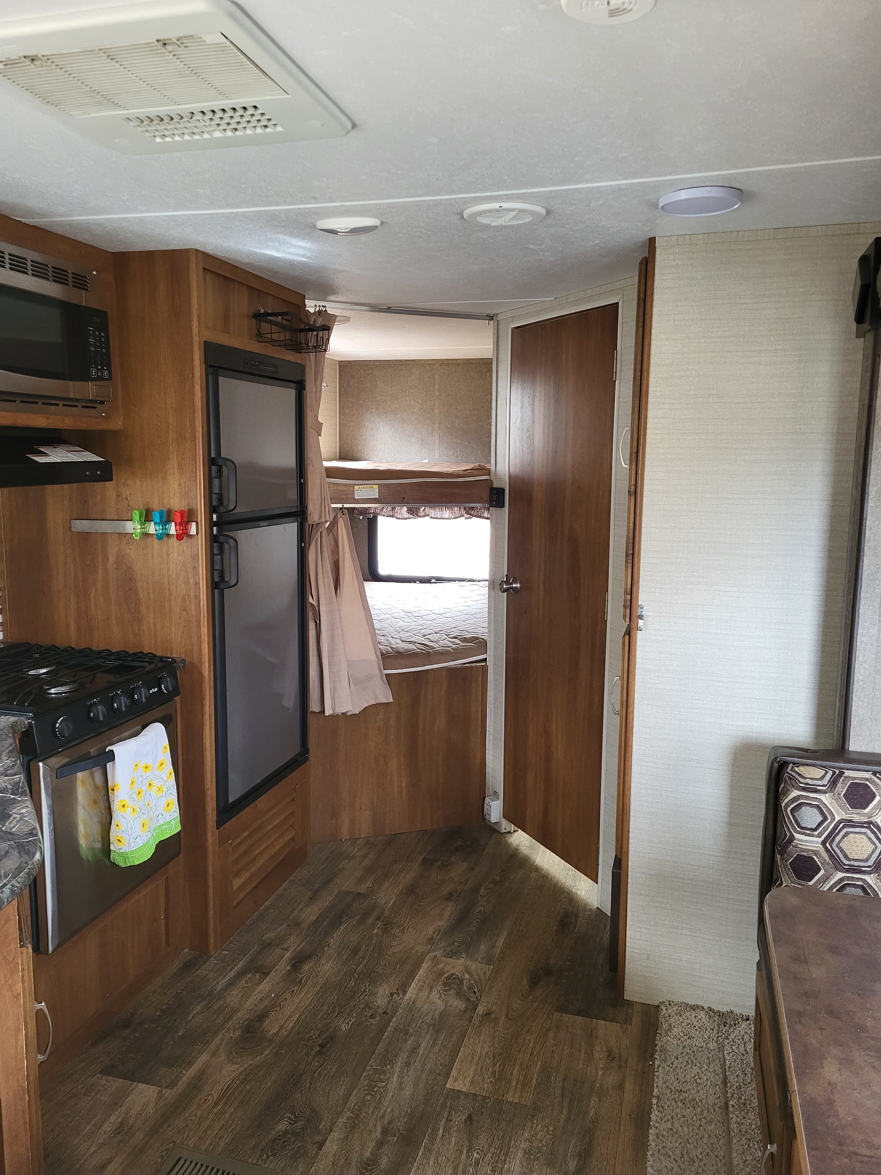 Spacious rv rental interior with kitchen (microwave, stove, fridge), bunk beds, and dining area with wood-look flooring.. Keystone RV Springdale 2017